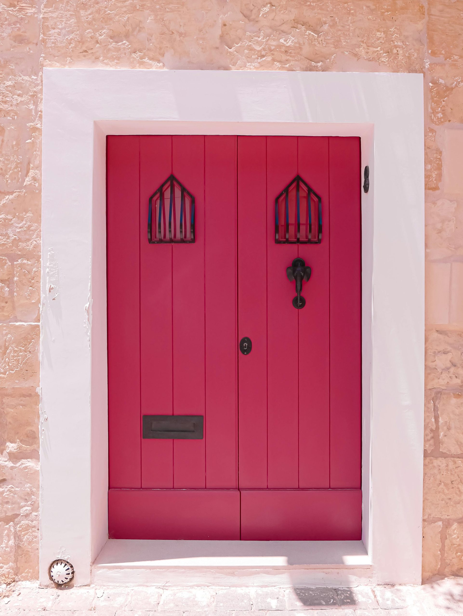 Bright pink door with antique knocker in a Maltese stone facade, capturing vibrant Mediterranean charm.