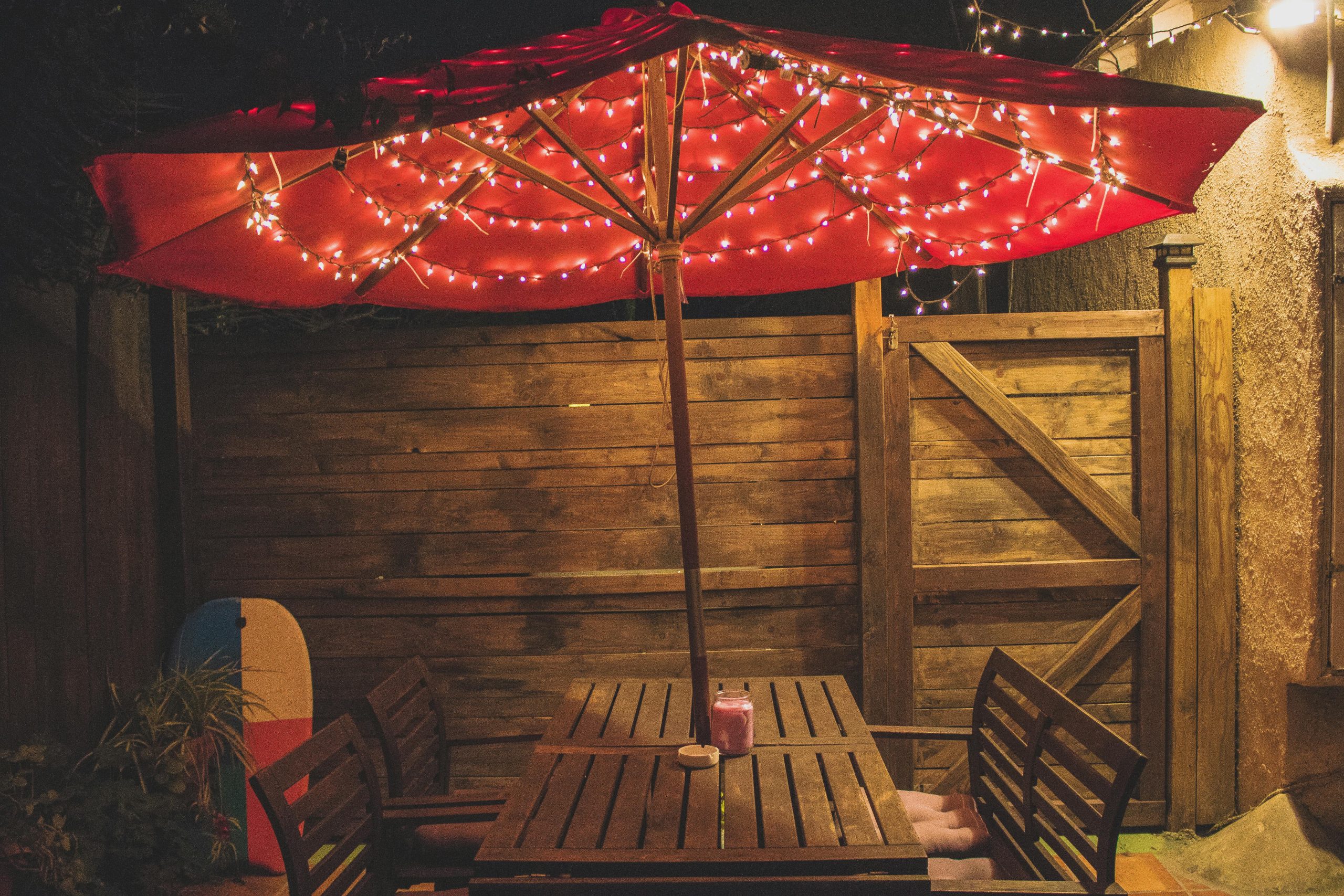 Charming outdoor dining setup with red parasol and string lights, perfect for evening gatherings.