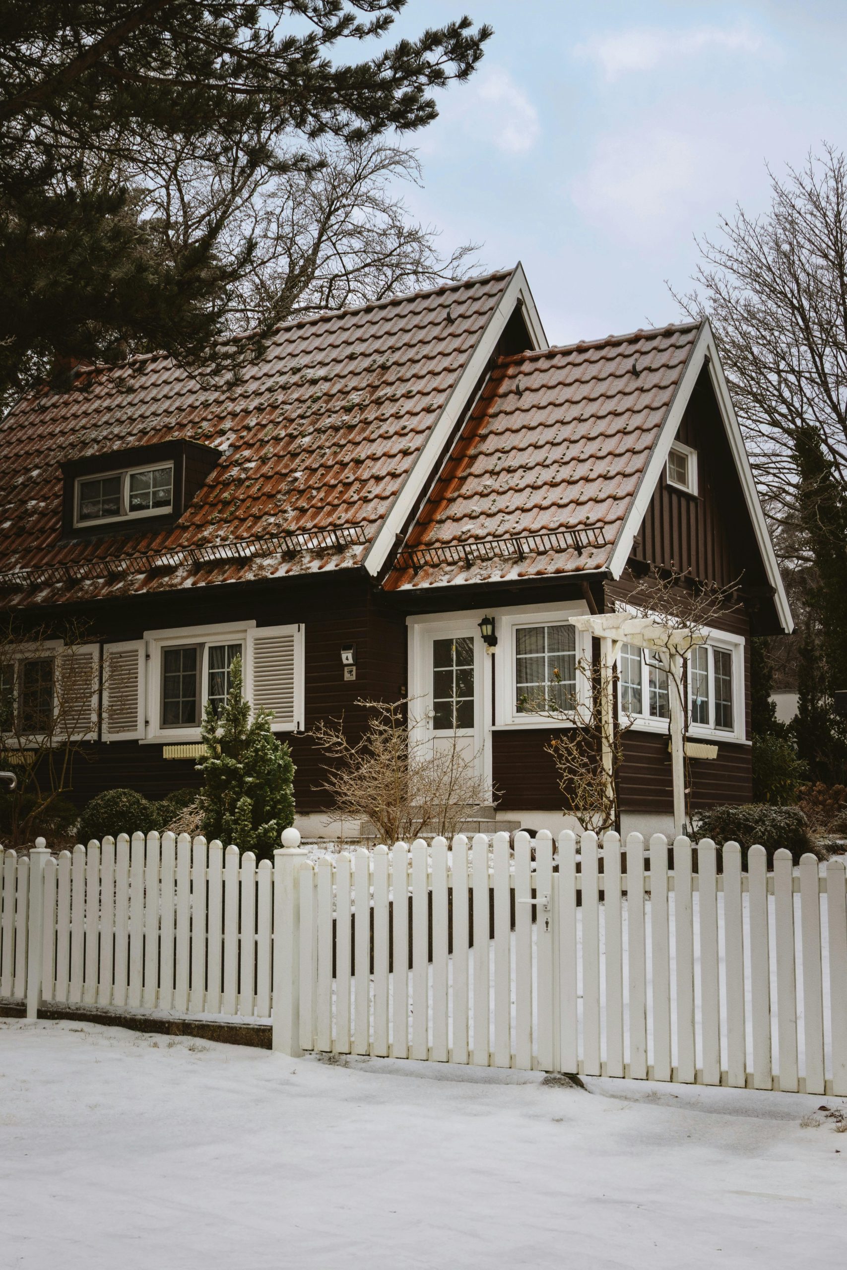 Idyllic winter scene featuring a snow-covered cottage with a wooden fence, surrounded by bare trees.