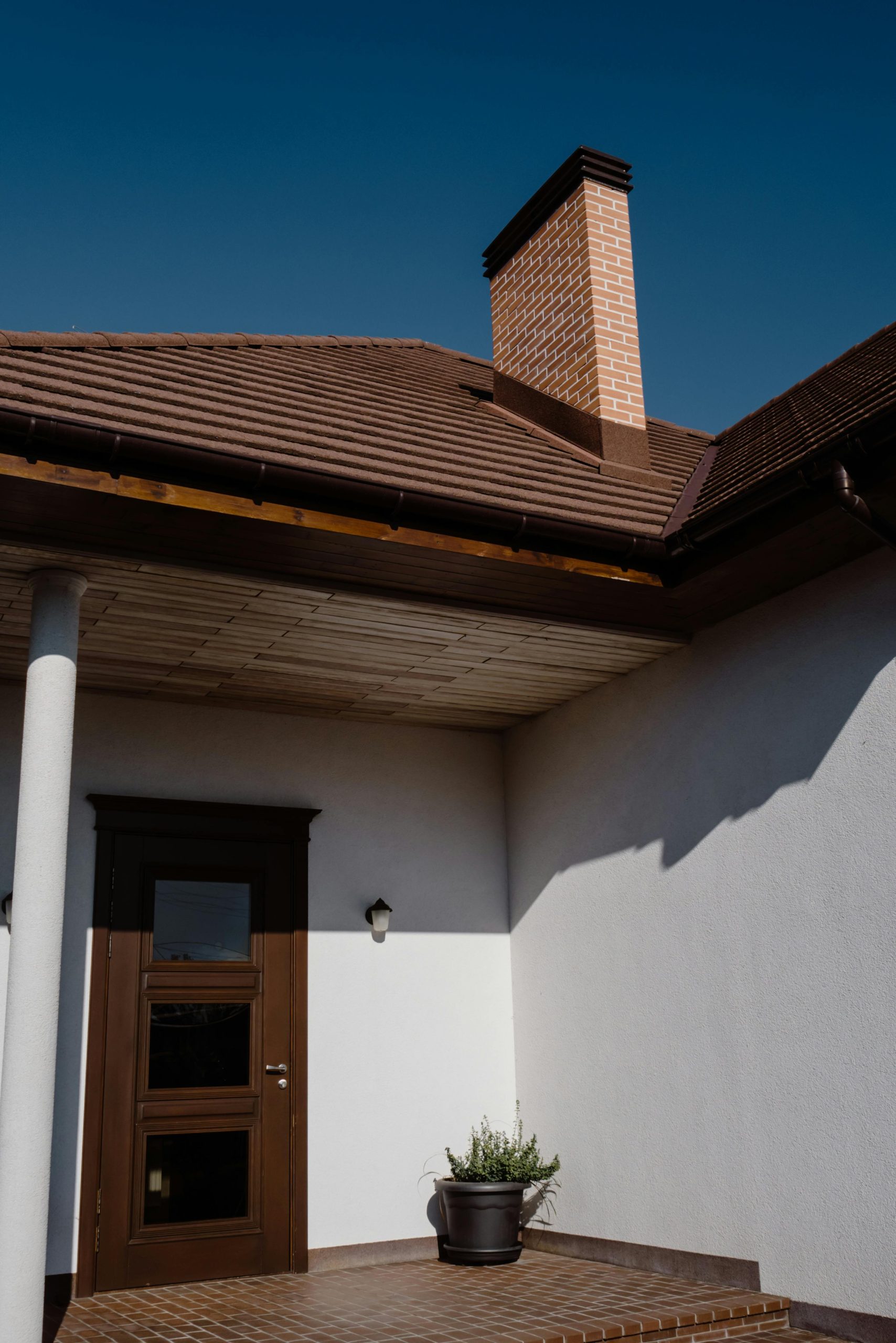 Modern house entrance featuring a wooden door and brick chimney under clear skies.