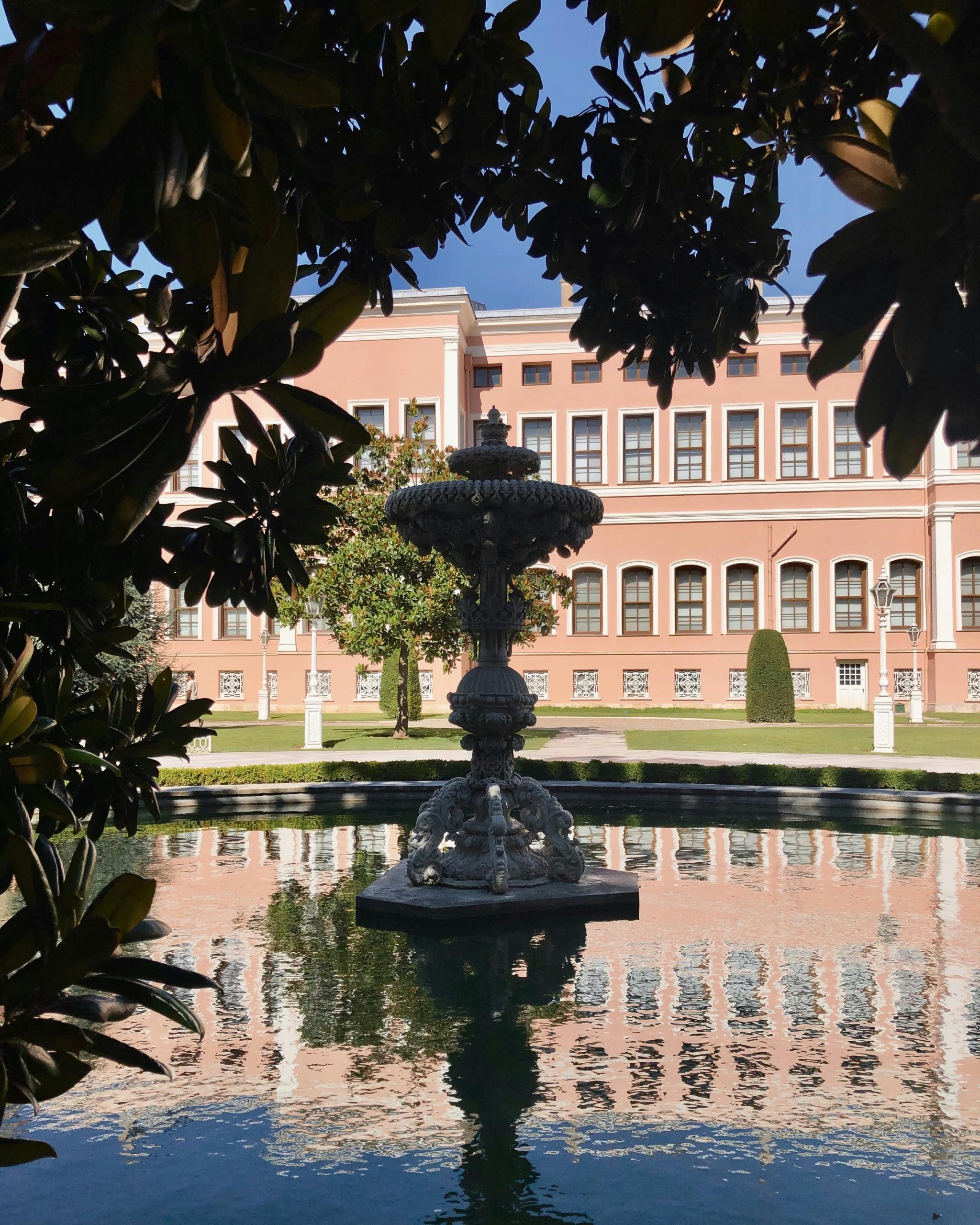 A beautiful fountain framed by trees in a lush garden with a historic building in the background.