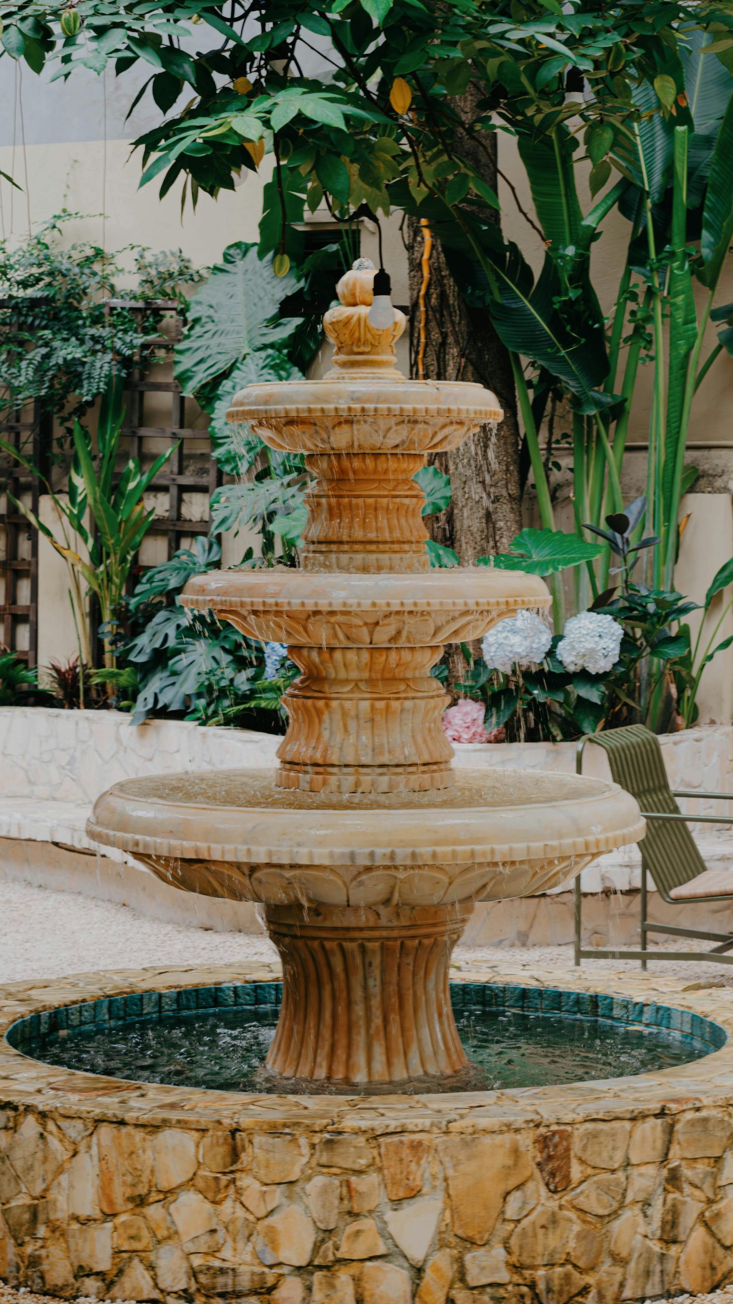 A beautiful three-tier stone fountain surrounded by lush greenery in an outdoor garden.