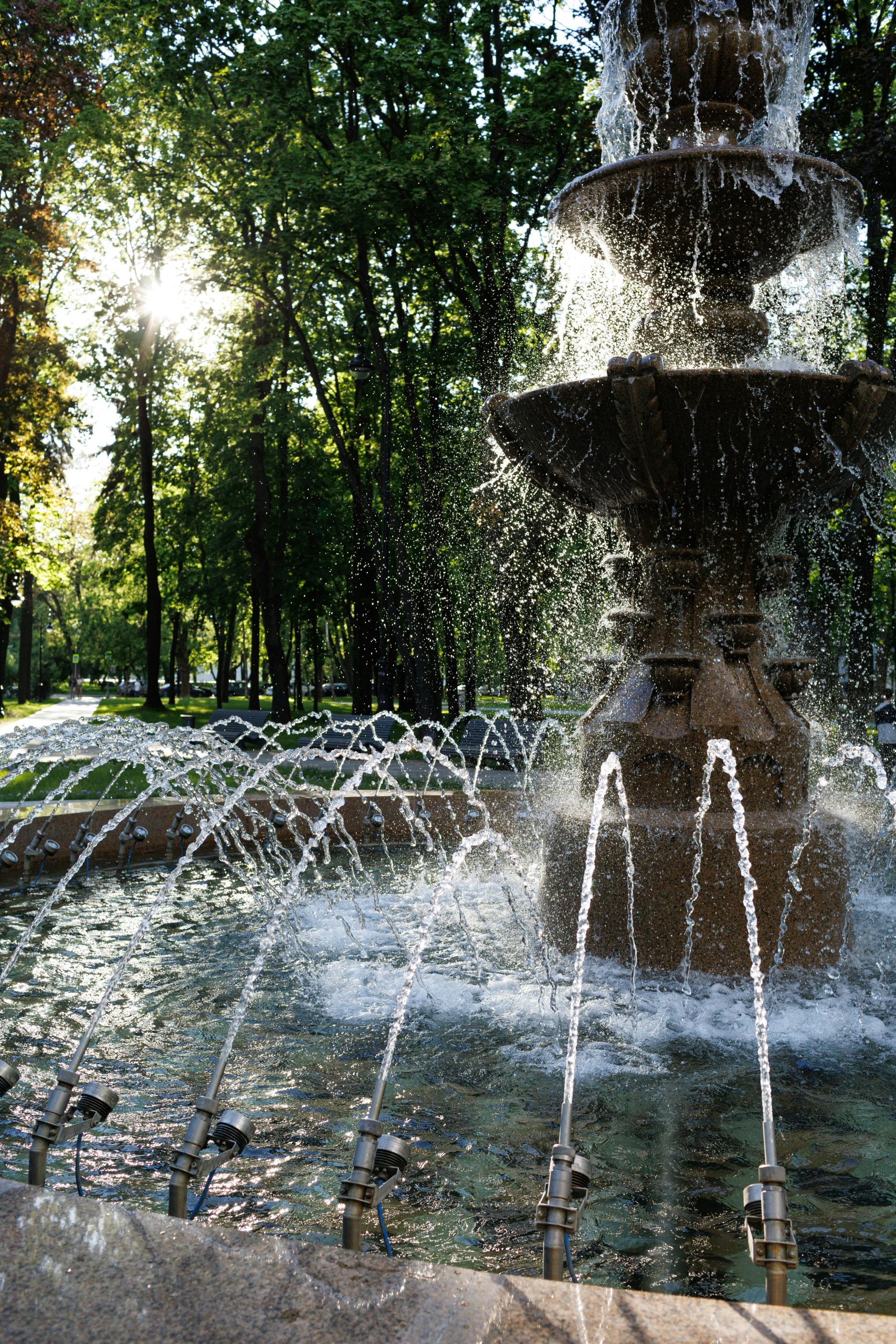 A breathtaking view of a stone fountain in a serene, sunlit park surrounded by lush greenery.