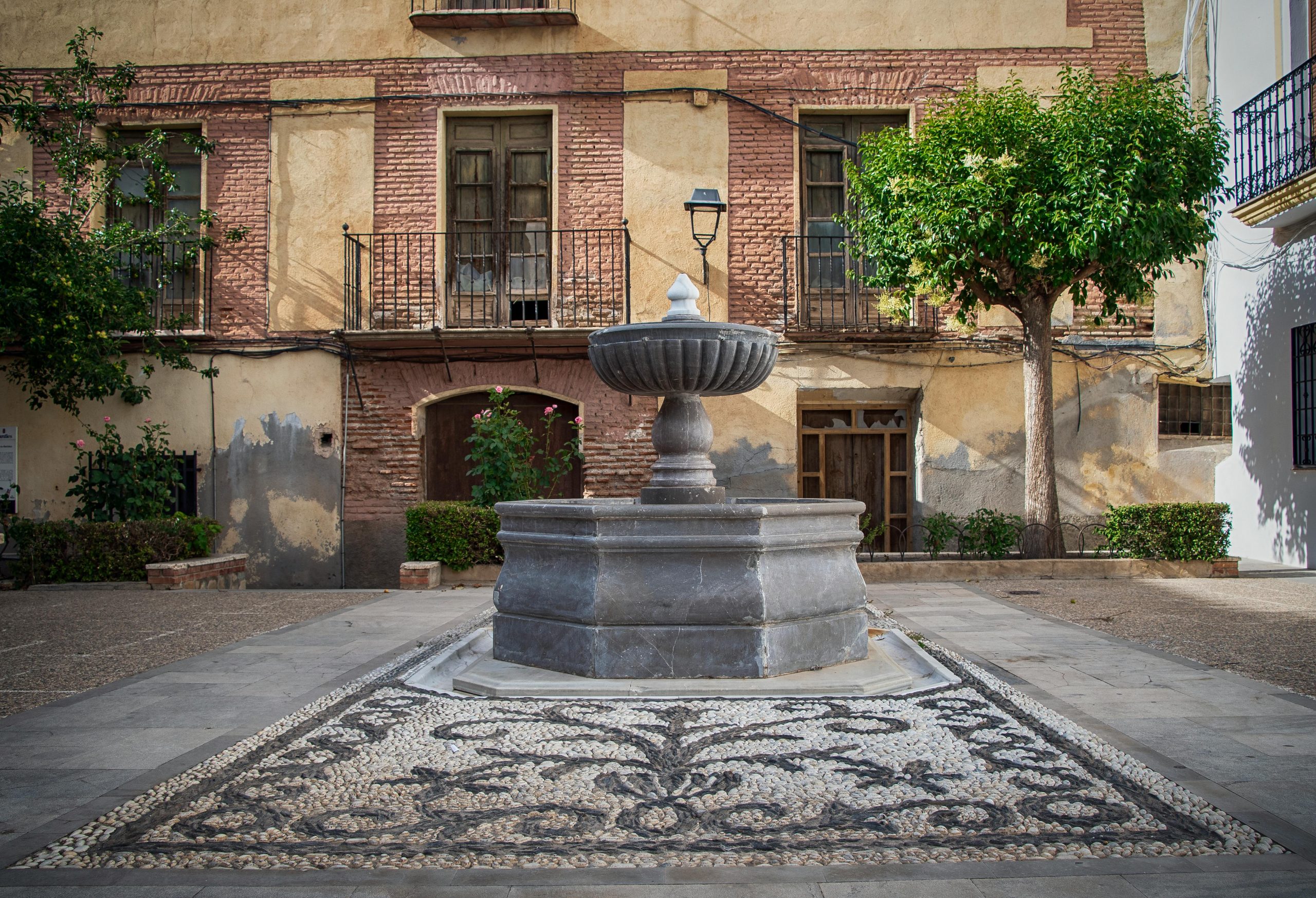 A picturesque courtyard featuring a central stone fountain surrounded by rustic architecture and greenery.