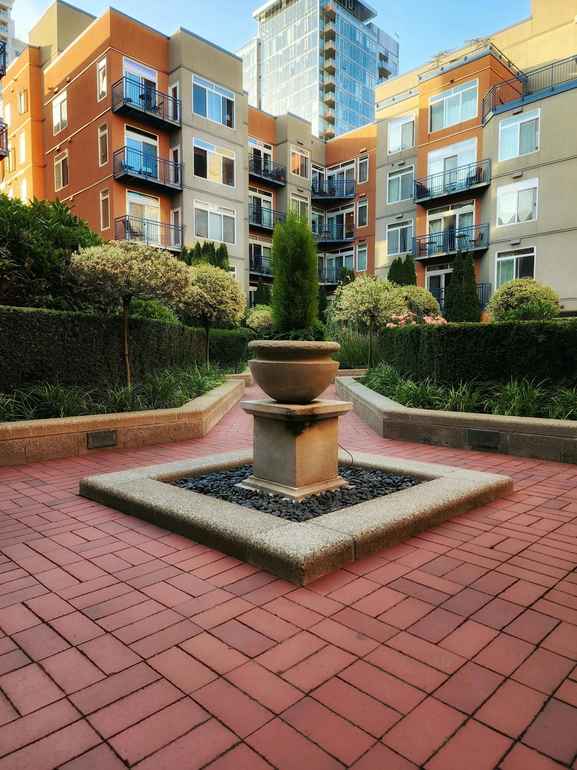 Beautiful courtyard garden with central stone fountain, surrounded by modern residential buildings.
