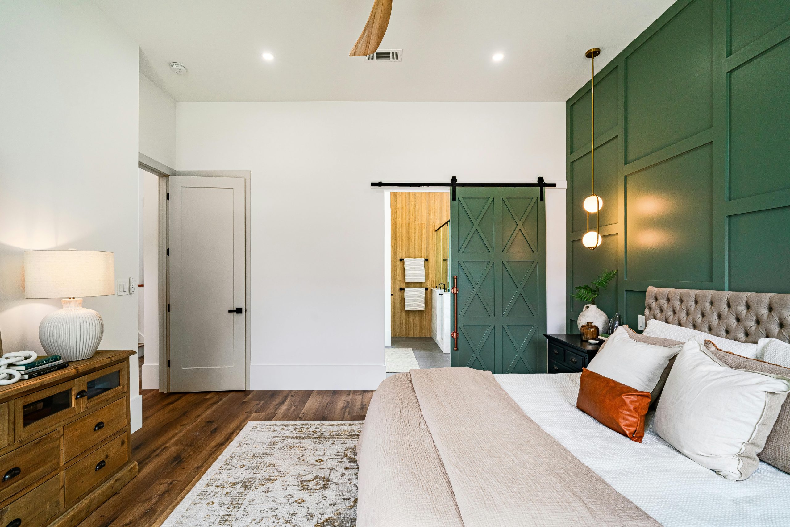 Beautiful modern bedroom with green accent wall and barn door leading to the bathroom.