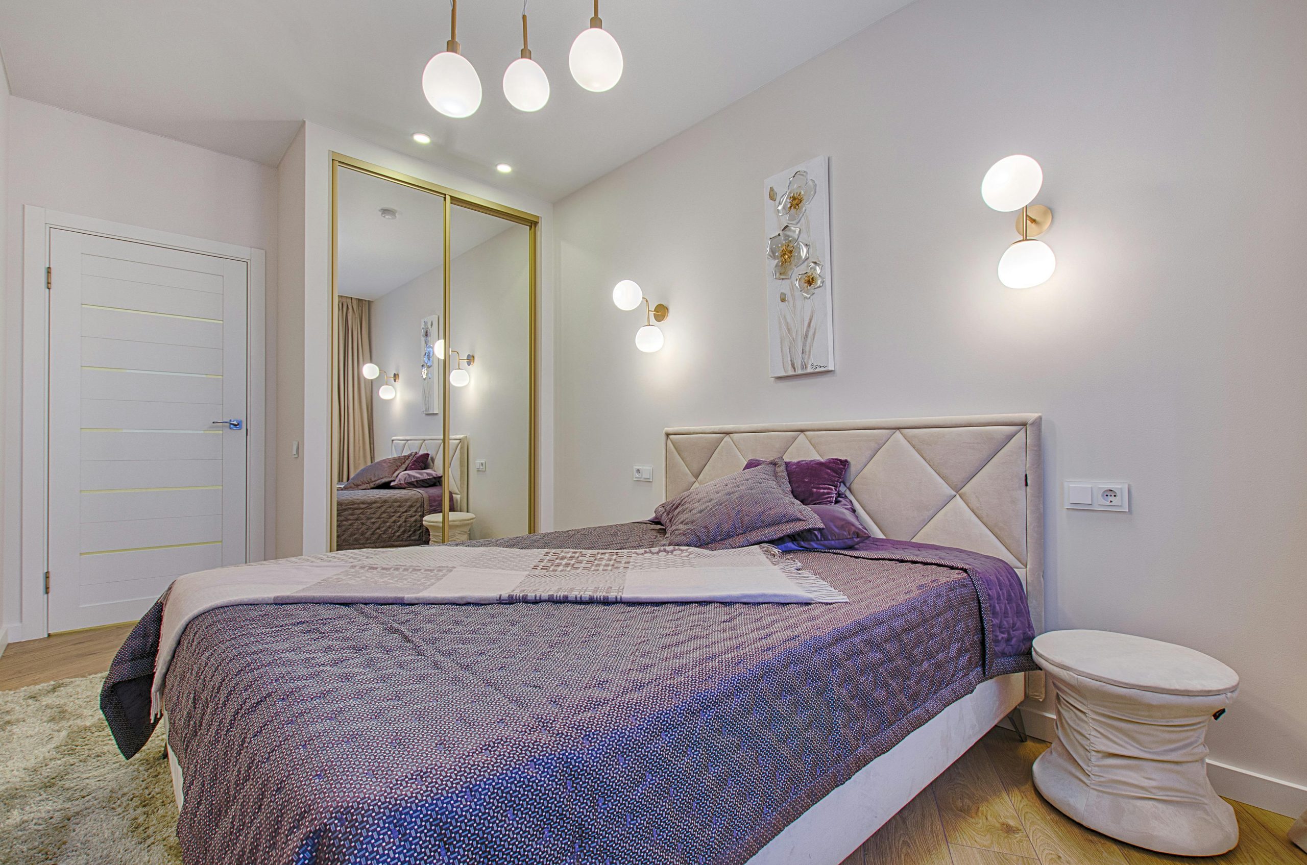 Elegant bedroom with purple decor, modern lighting, and mirror wardrobe.