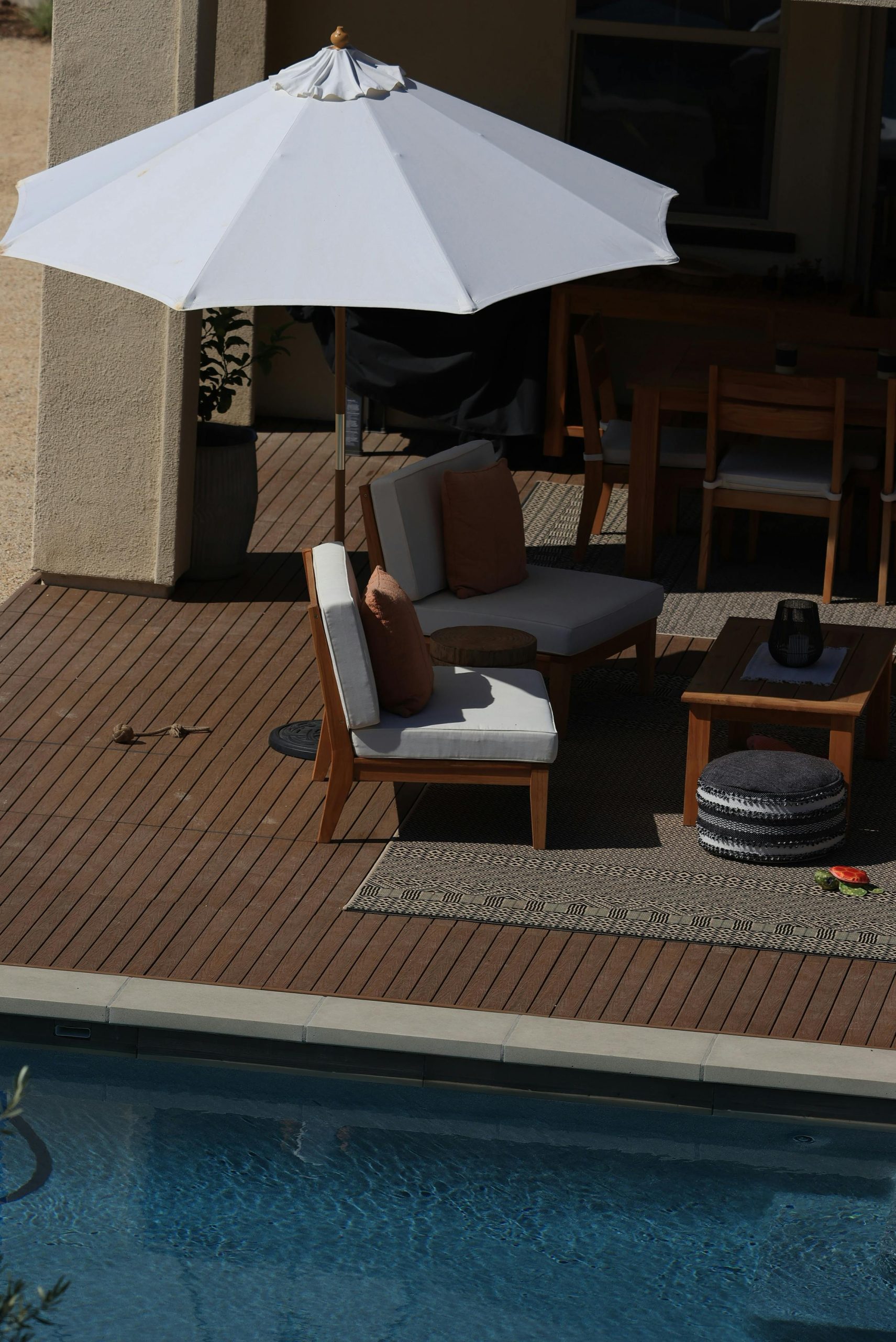 Elegant patio furniture under an umbrella by a clear swimming pool, ideal for summer relaxation.