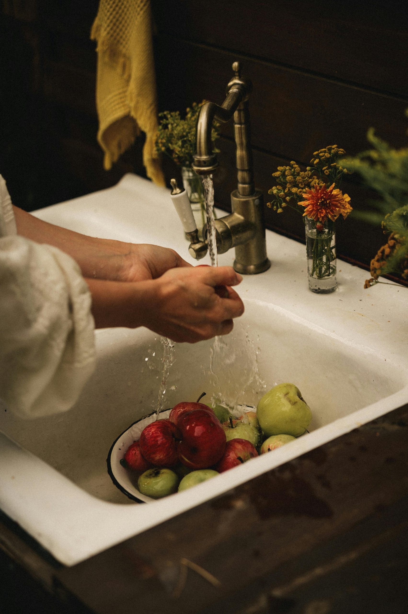Hands washing apples in a vintage sink with rustic decor, evoking a homely autumn feel.