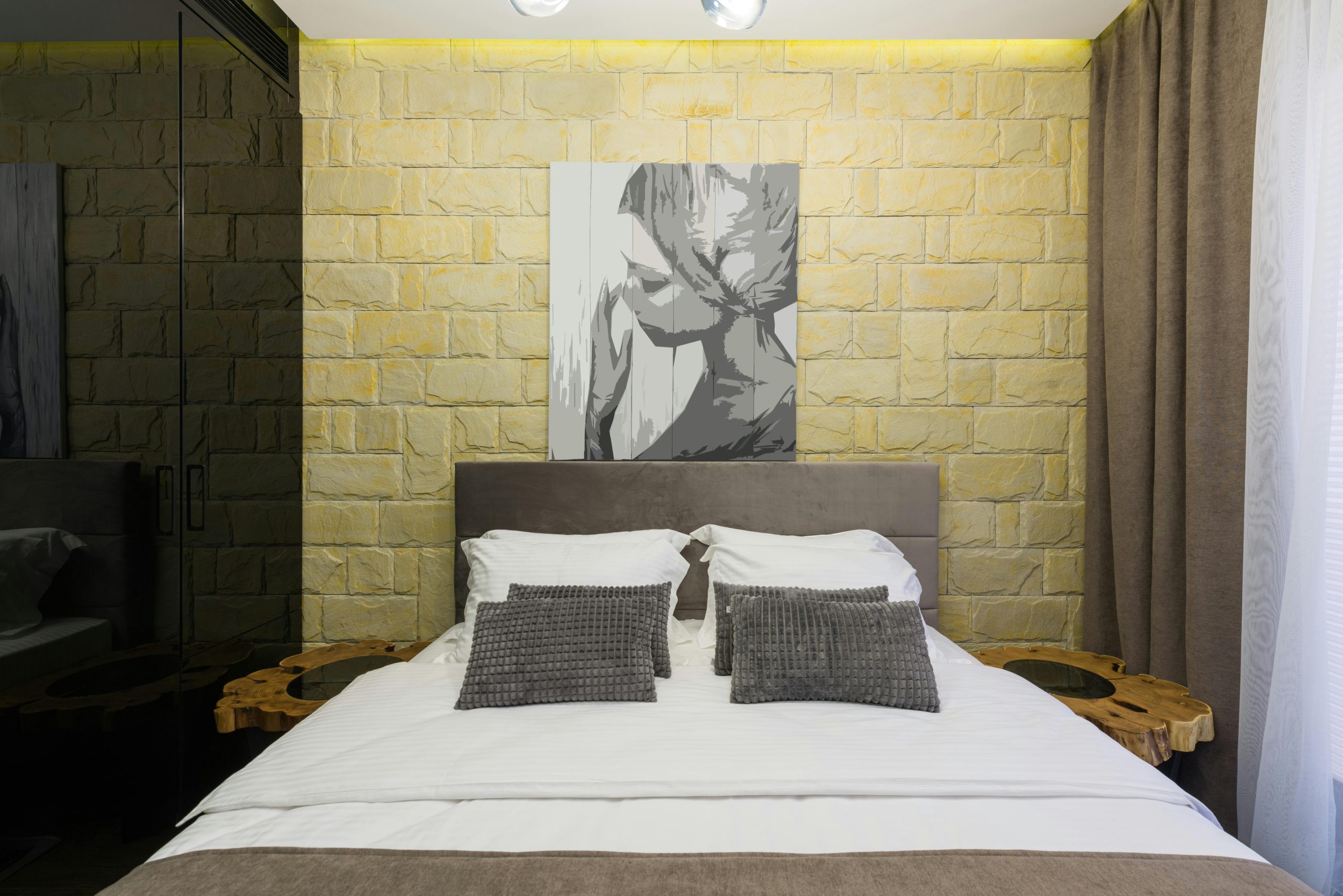 Loft style bedroom with soft cushions on bed against rough wall with artwork in hotel