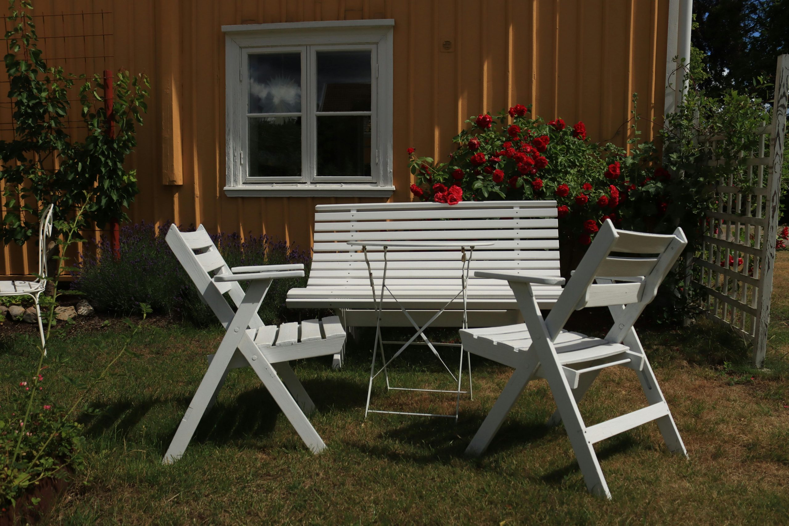 Outdoor seating area with white furniture surrounded by blooming red roses in Huskvarna, Sweden.