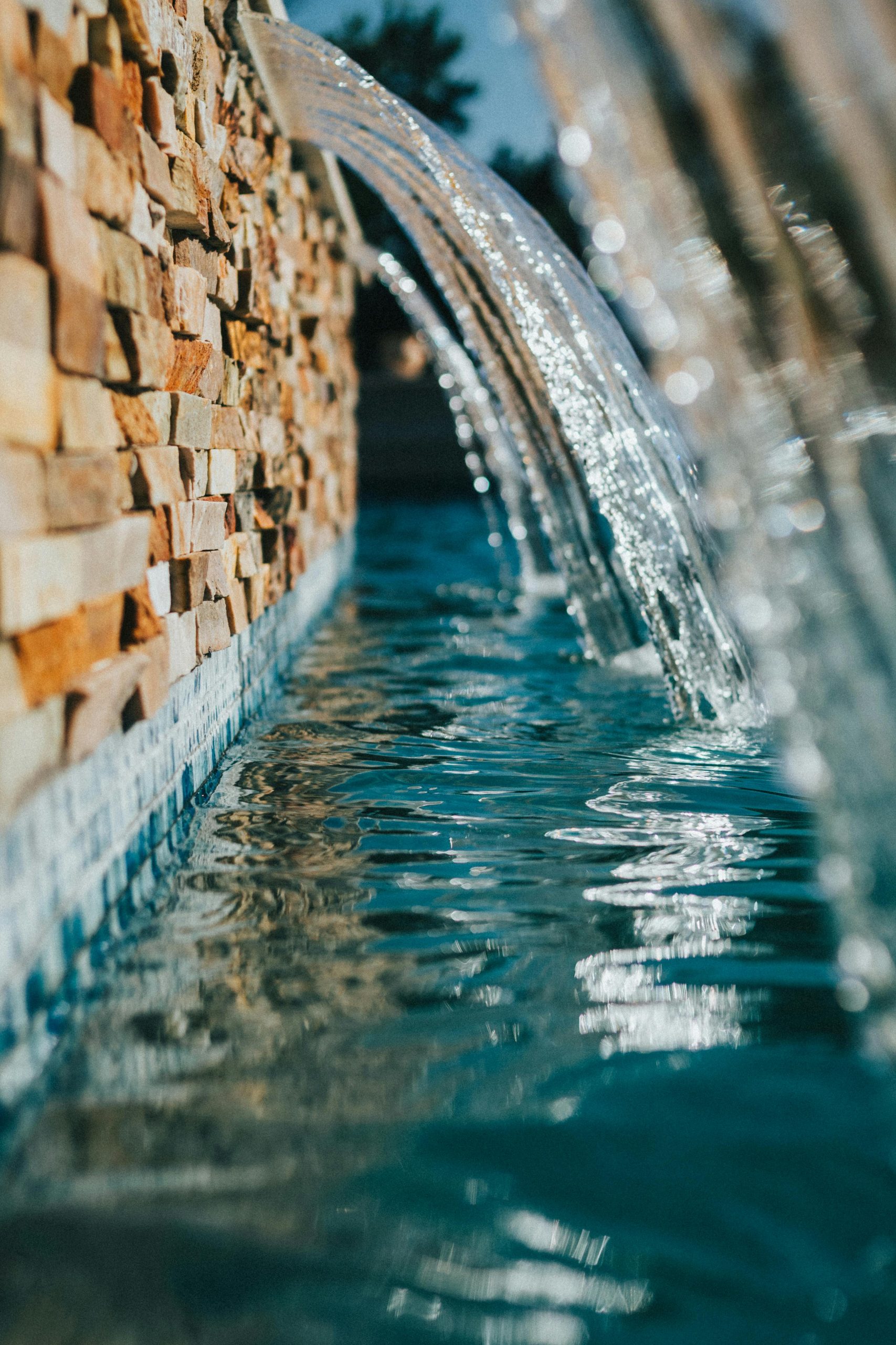 Refreshing waterfall flowing from a stone wall into a serene pool outdoors. Perfect for tranquility concepts.