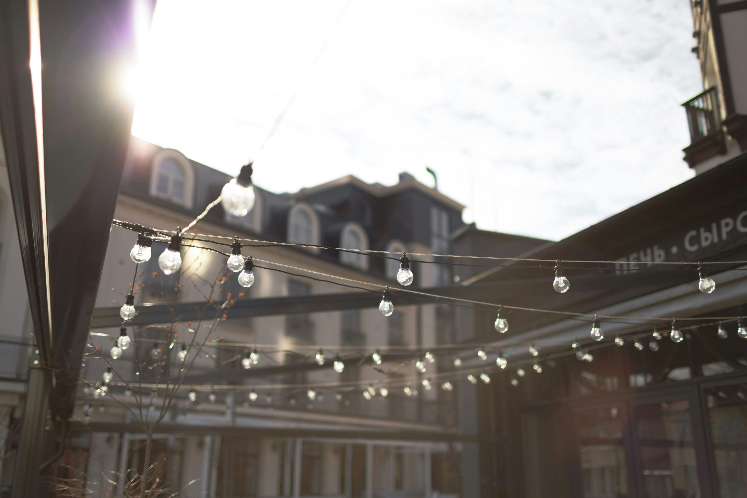 String lights hang outside buildings under bright sun.