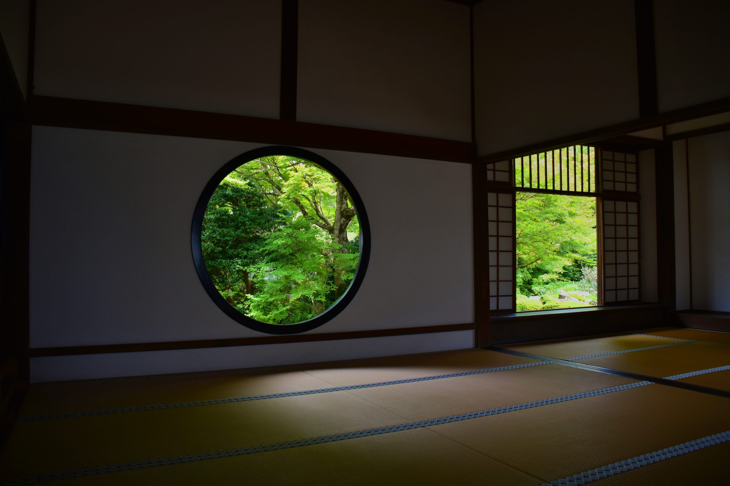 Traditional japanese room with circular window overlooking lush greenery.