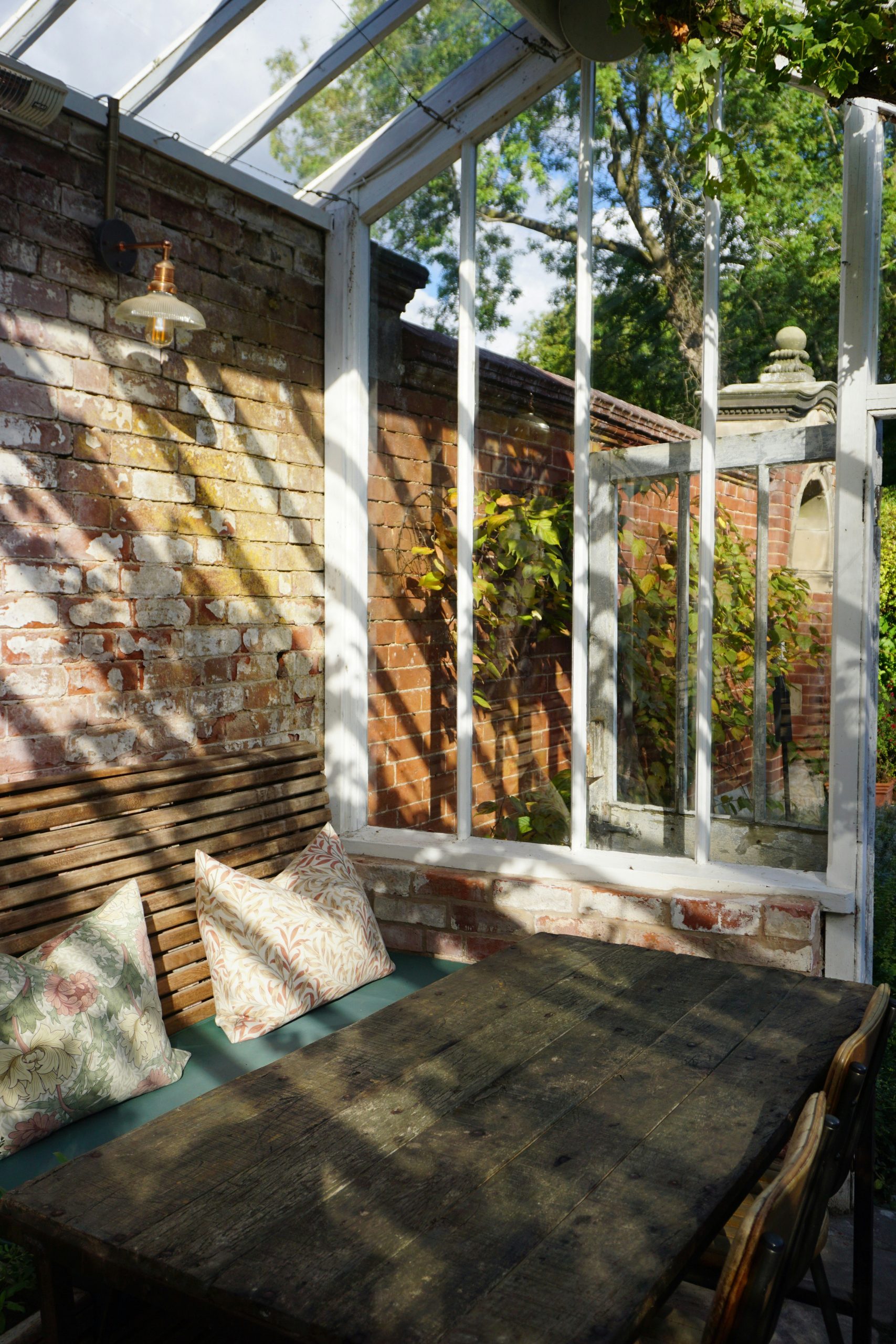 Wooden table and chairs in a sunlit greenhouse.