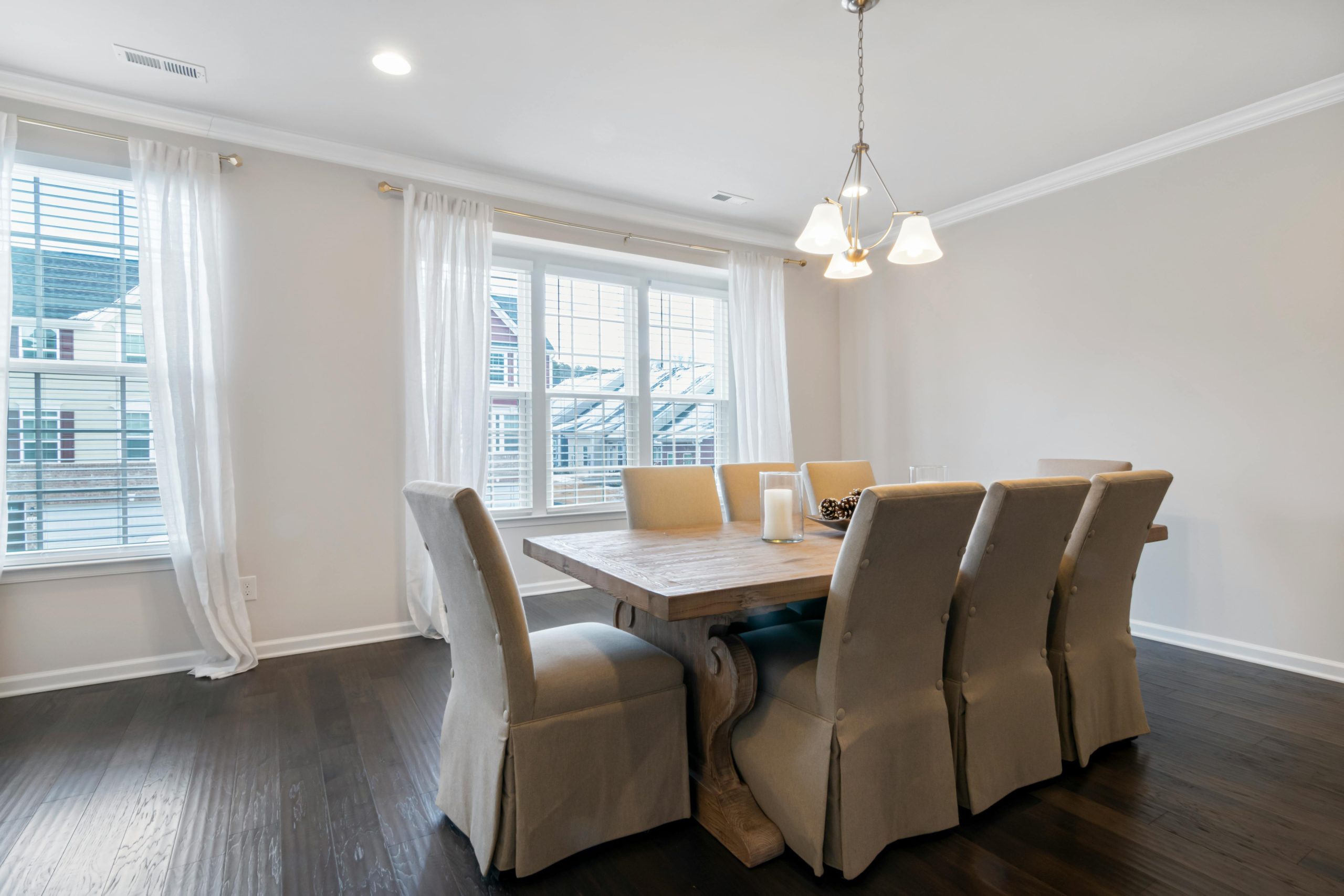 A bright dining room featuring a wooden table, upholstered chairs, and elegant lighting.