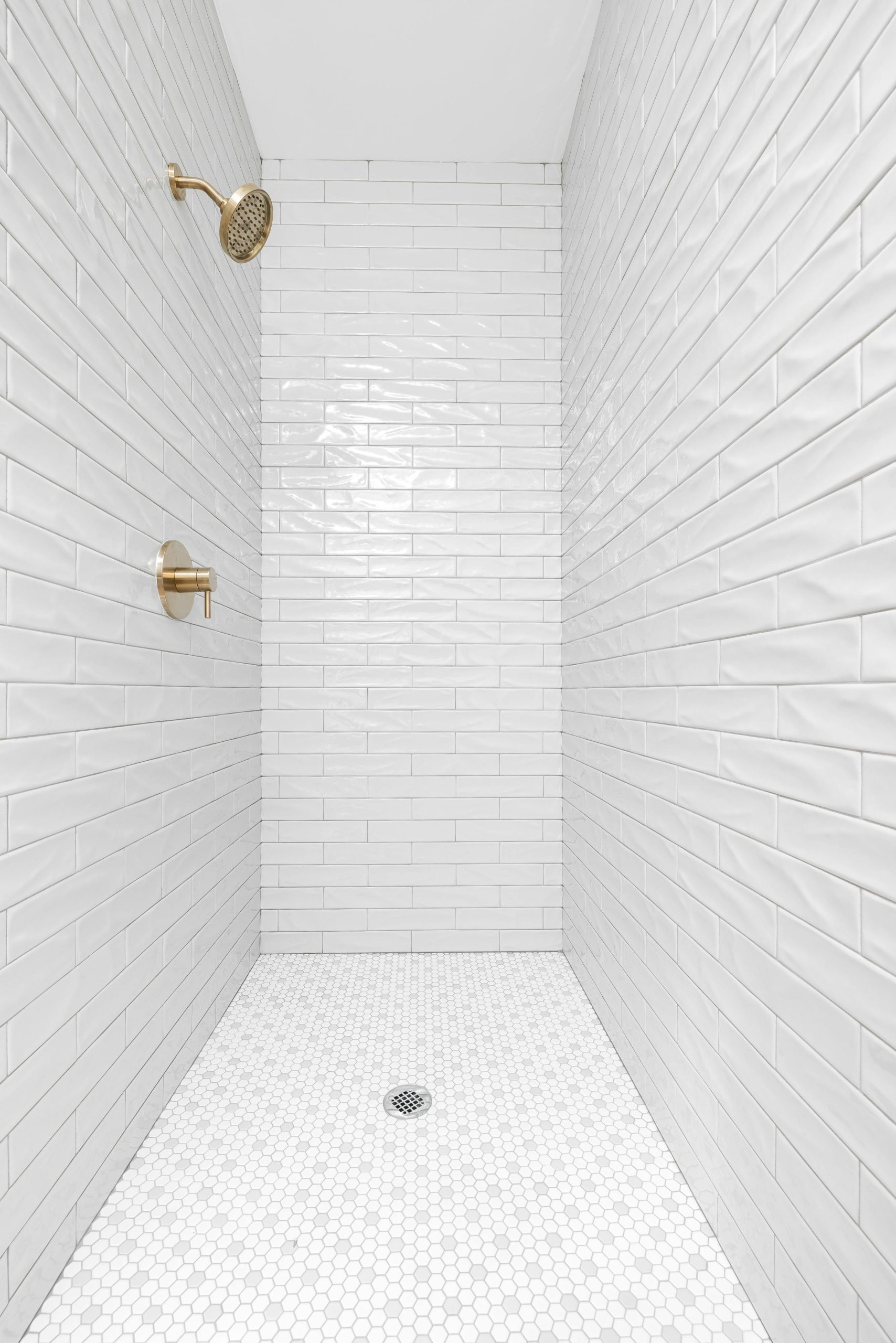 A clean, minimalist bathroom shower featuring white tiles and brass fixtures.