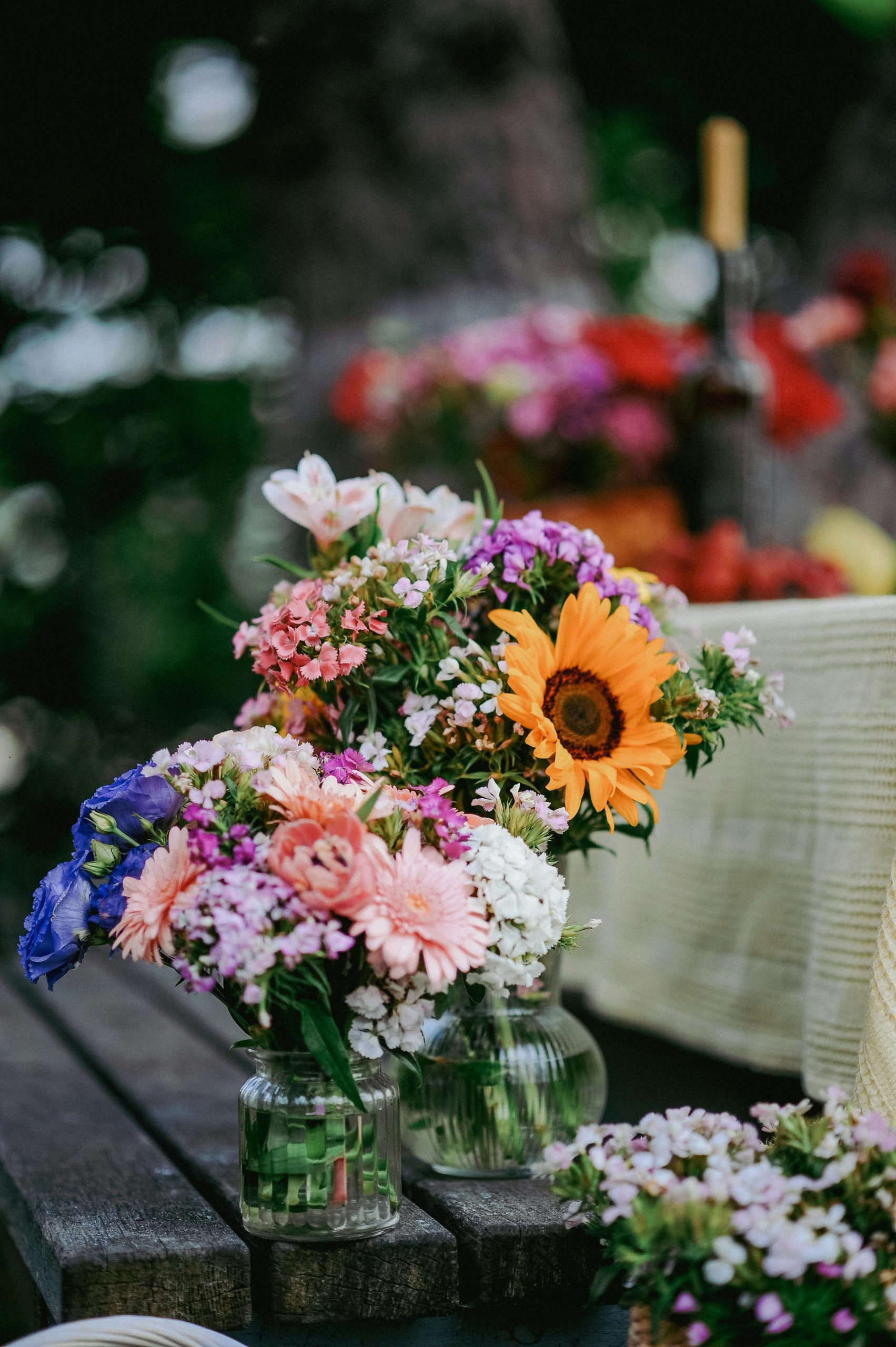 A colorful bouquet of summer flowers in a glass jar on a wooden table, outdoors.
