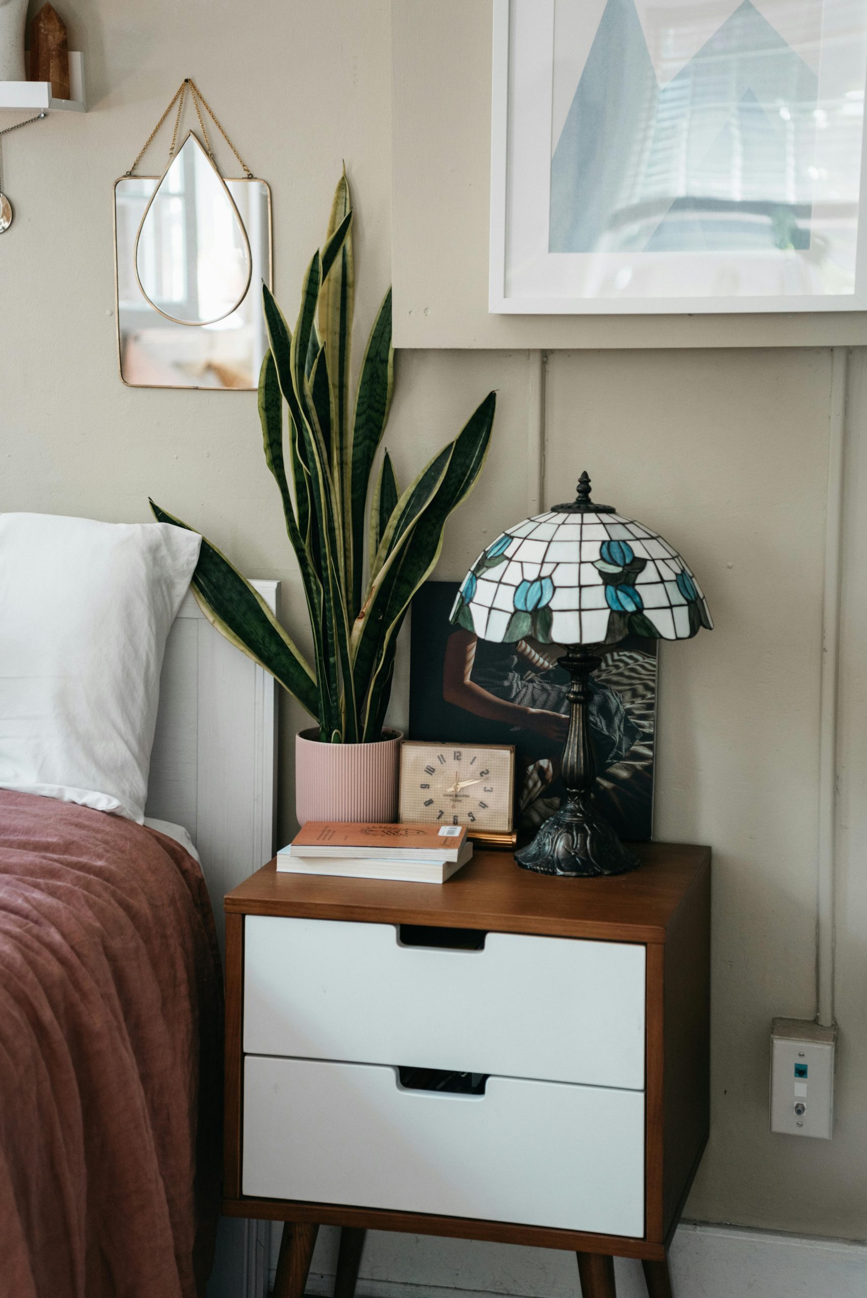 A minimalist bedroom featuring a stylish side table, snake plant, and decorative lamp.