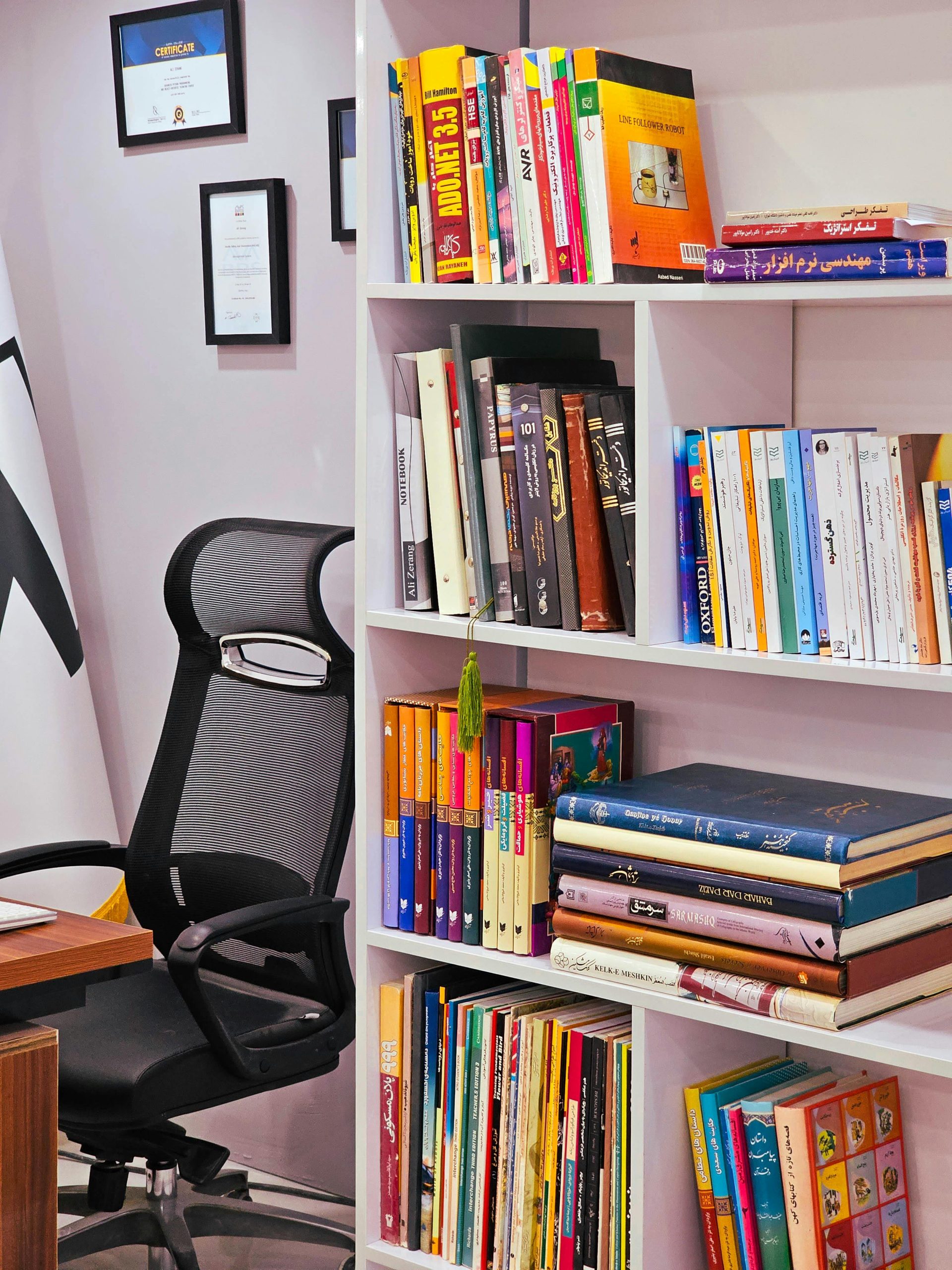 A modern office space with a bookshelf filled with colorful books and an ergonomic chair.