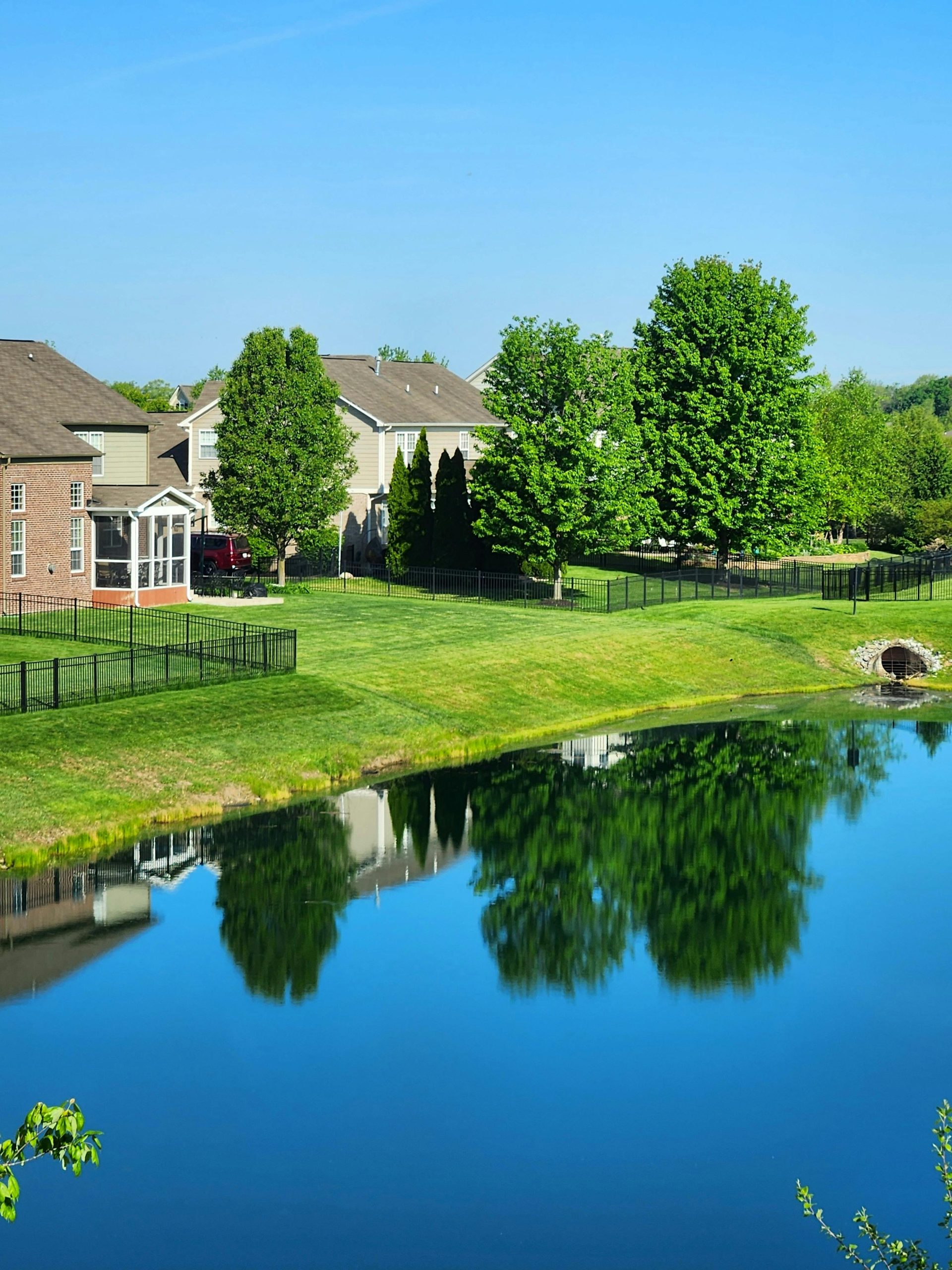 A scenic view of a suburban neighborhood with houses reflected in a calm pond under a clear blue sky.