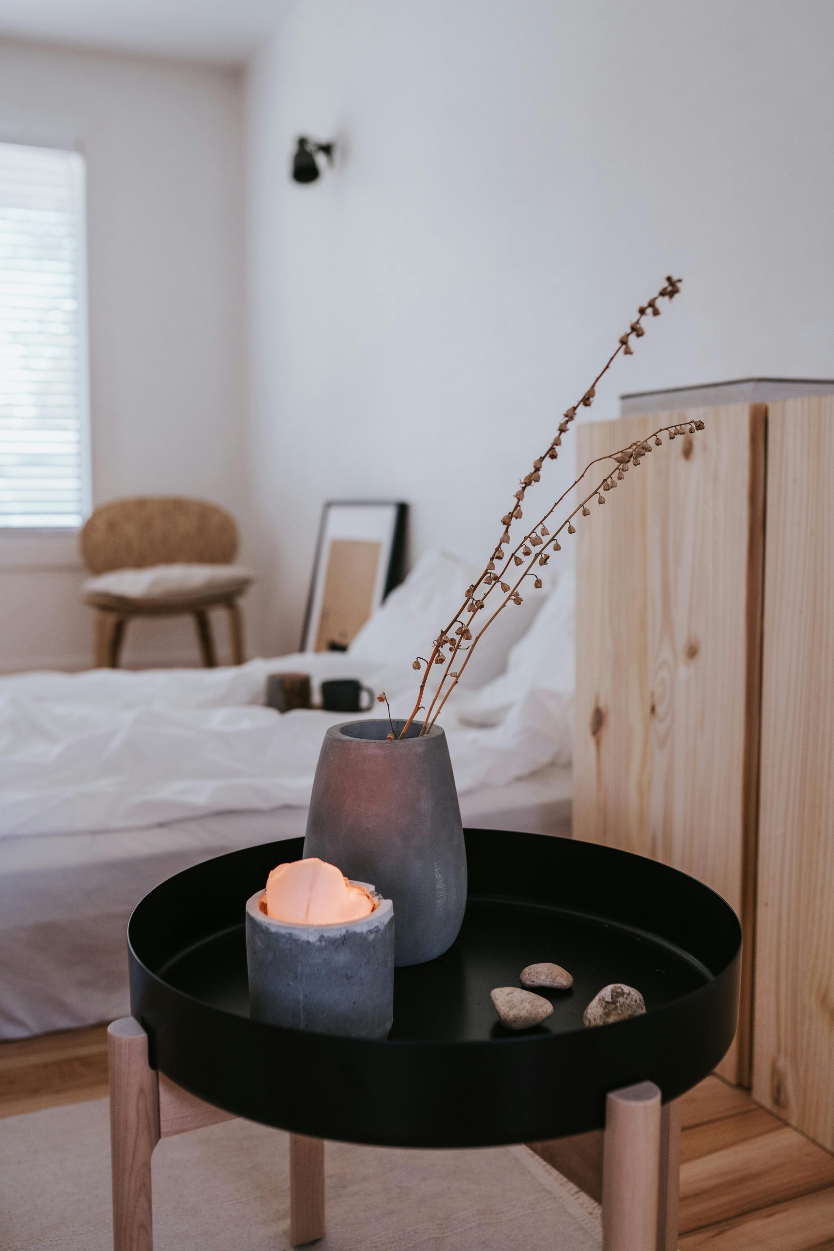 A serene Japandi-style bedroom showcasing minimalist decor with a wooden cabinet, round table, and soft candlelight.