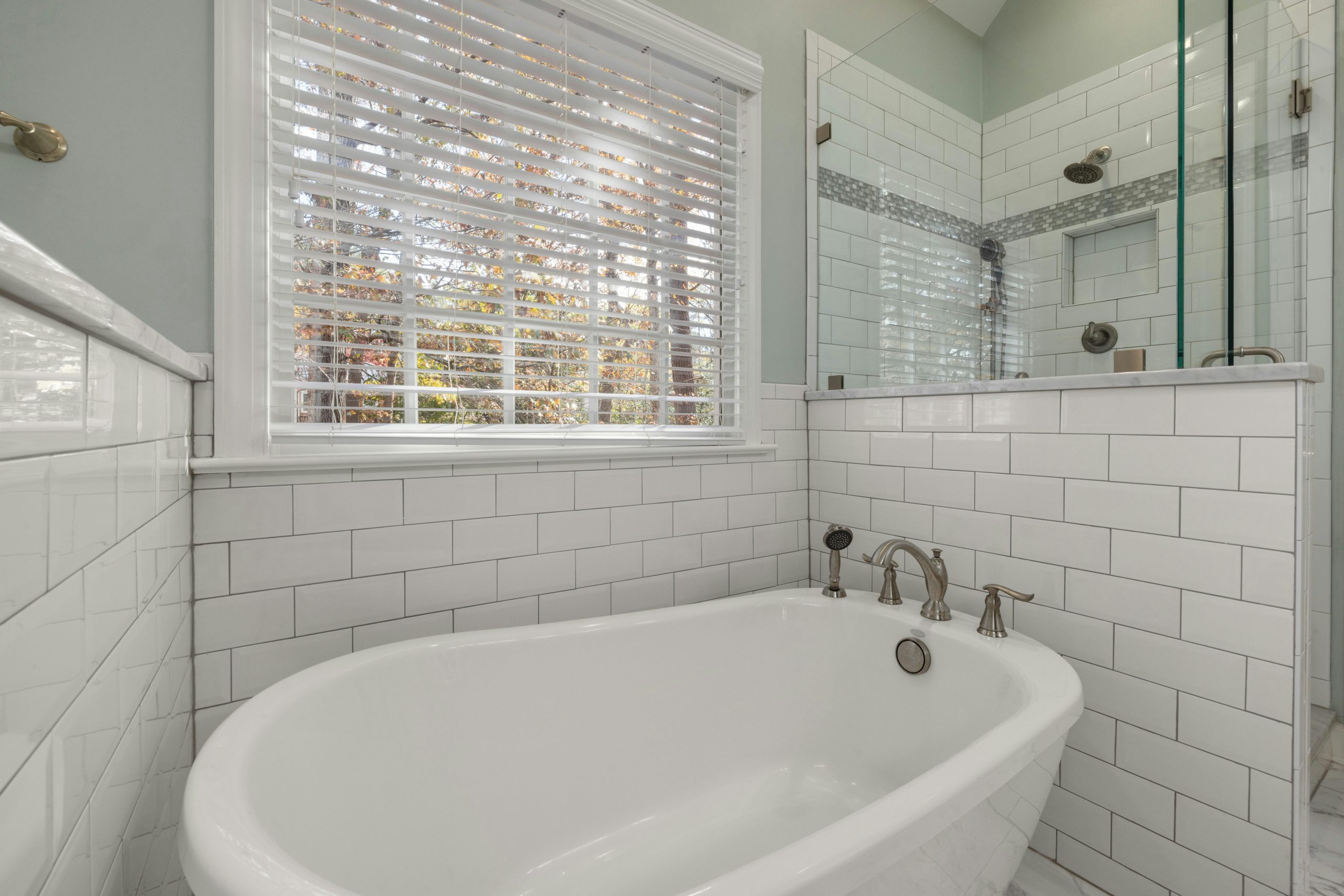 A spacious bathroom featuring a luxurious freestanding tub and glass shower surrounded by subway tiles.