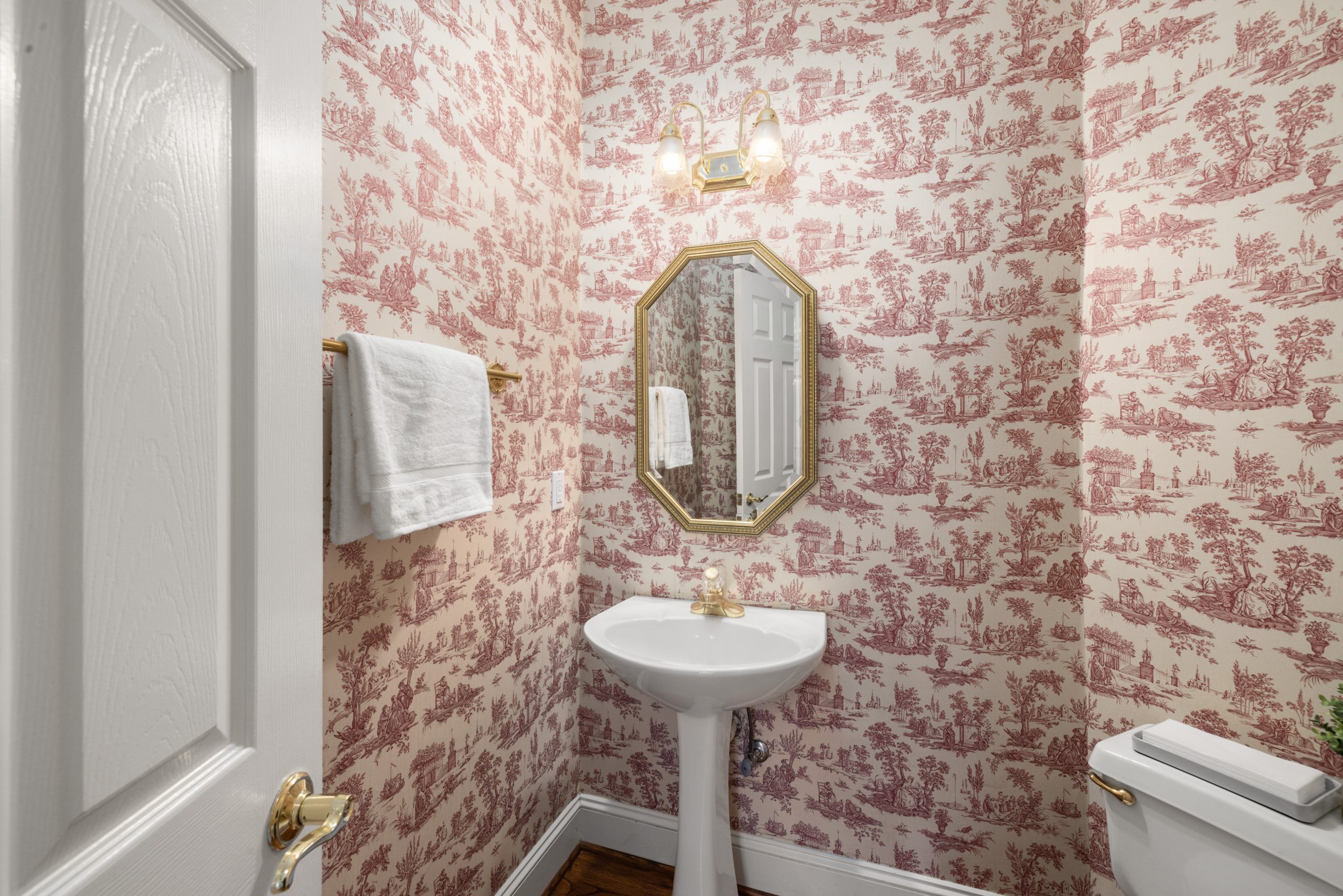 A stylish bathroom featuring vintage red wallpaper, elegant mirror, and white fixtures.