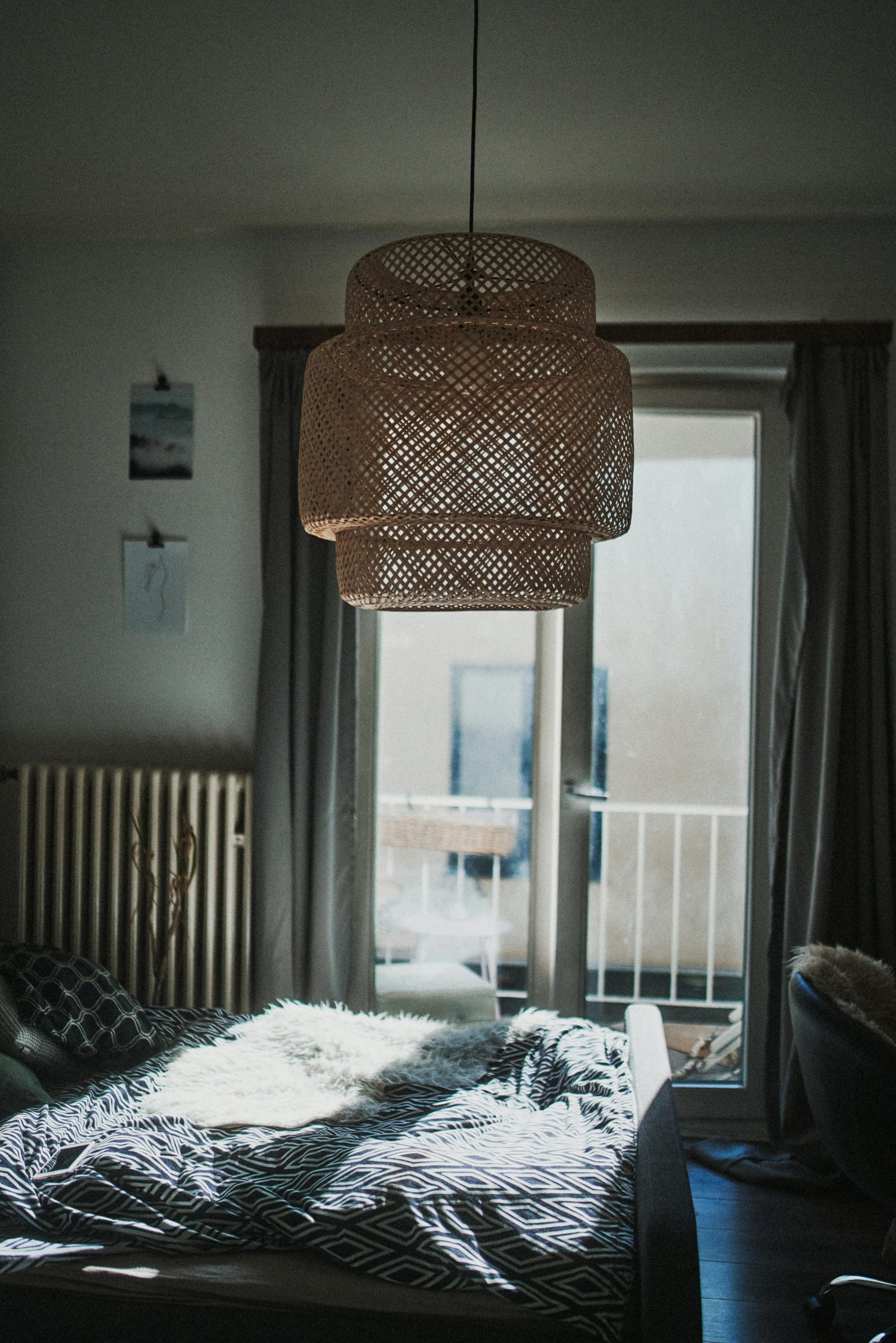 A well-lit bedroom featuring a woven pendant lamp above a bed with patterned bedding, capturing a tranquil atmosphere.