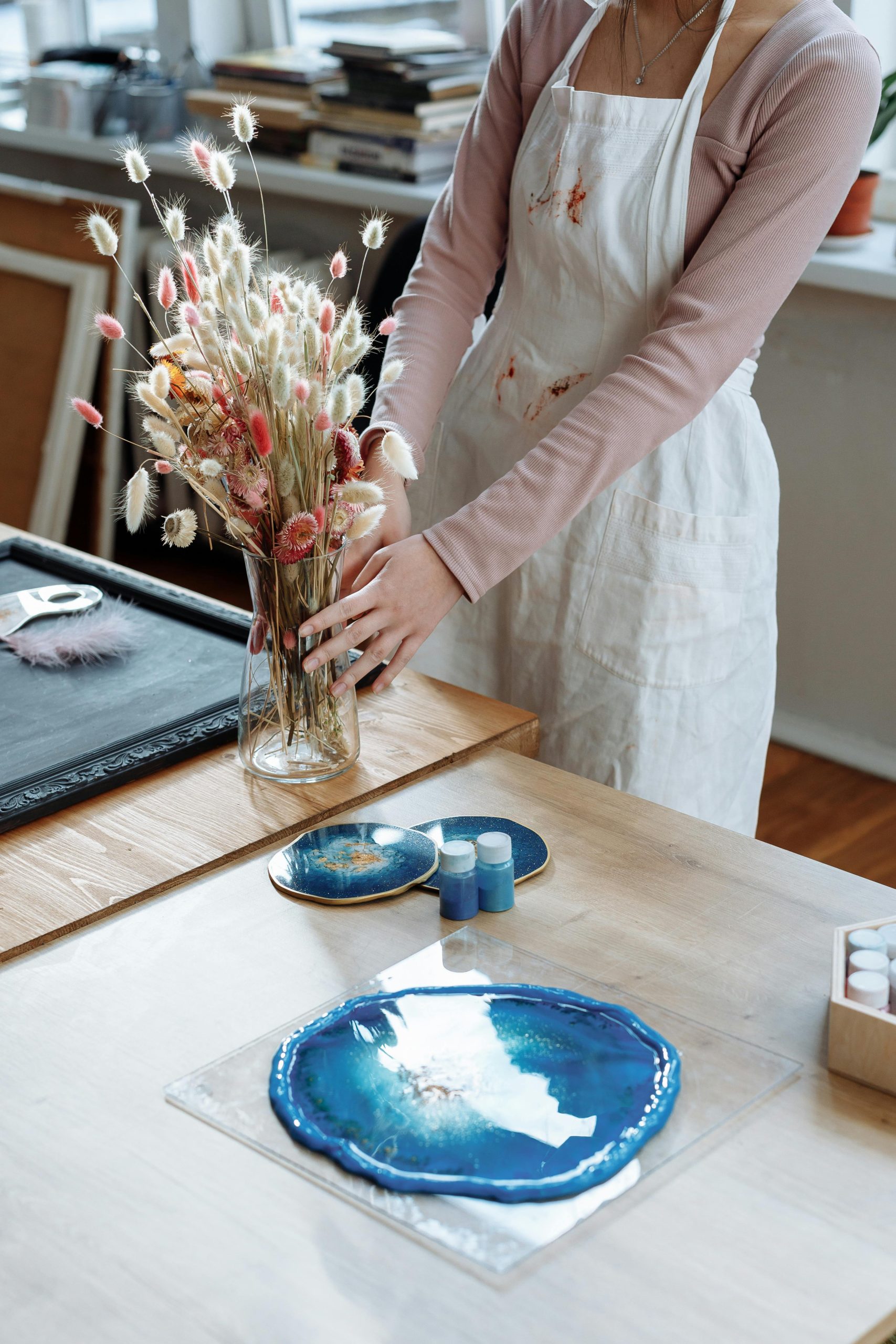 A woman in a studio arranges dried flowers on a table with artistic resin plates.