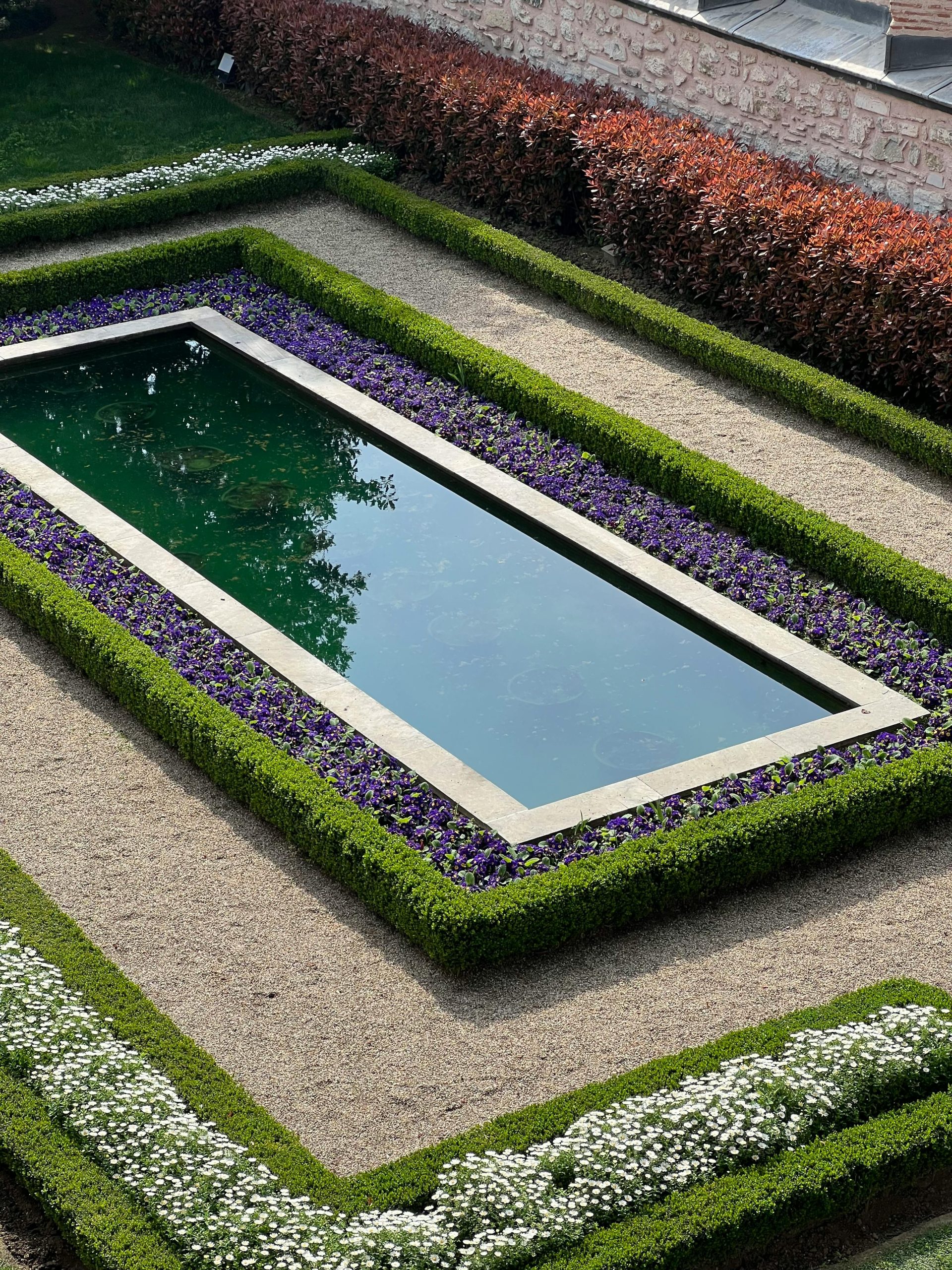 Aerial view of a rectangular reflecting pool surrounded by manicured hedges and vivid flowers.