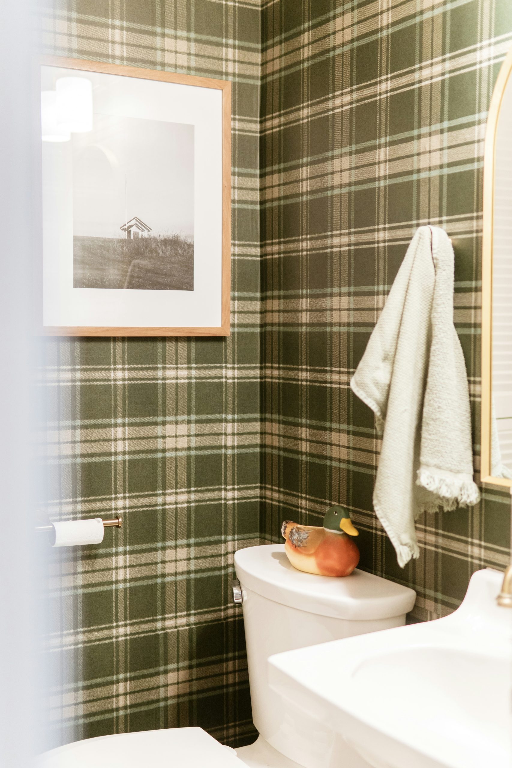 Bathroom with green plaid wallpaper and framed art.