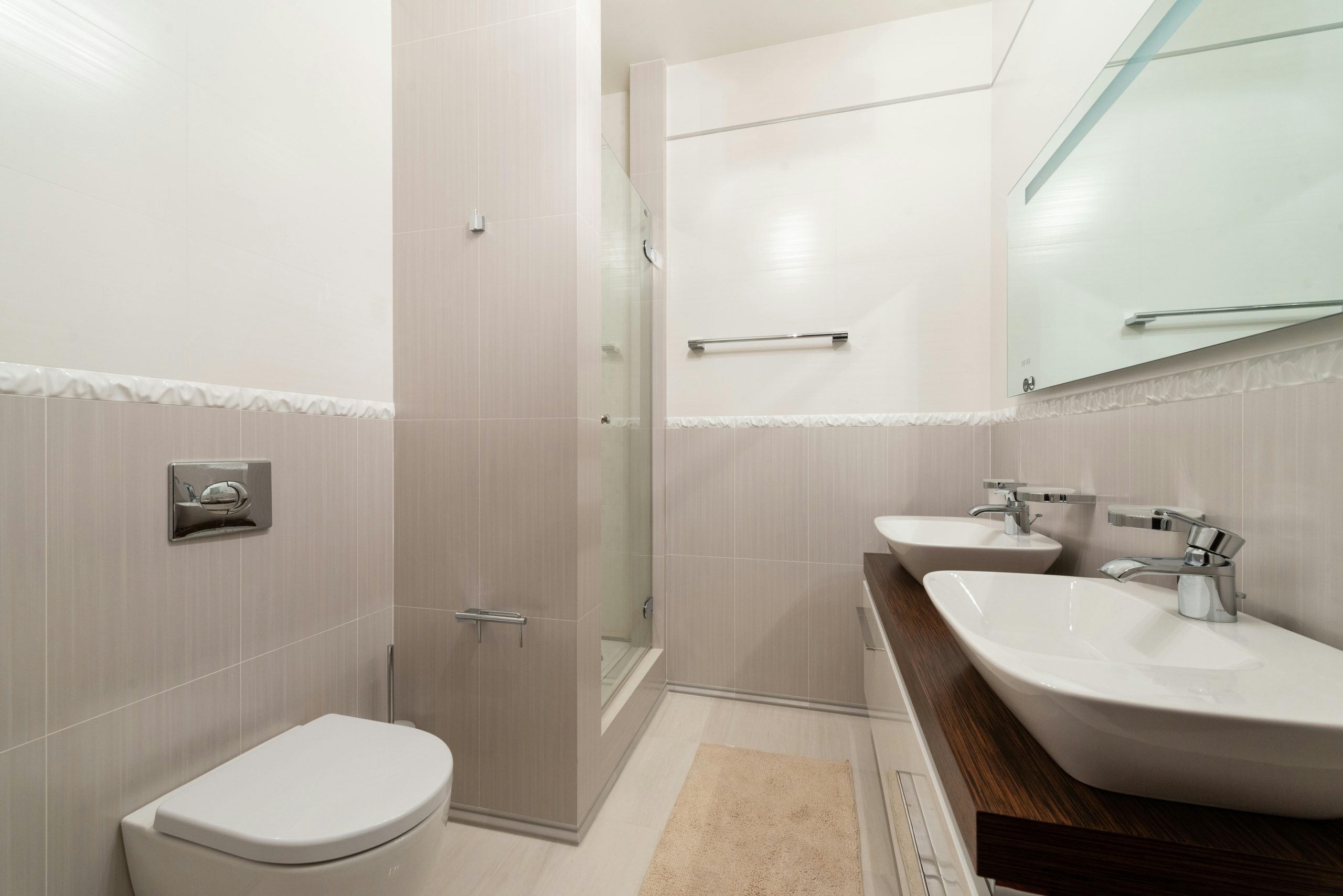 Bright and clean modern bathroom with shower, sinks, and toilet.