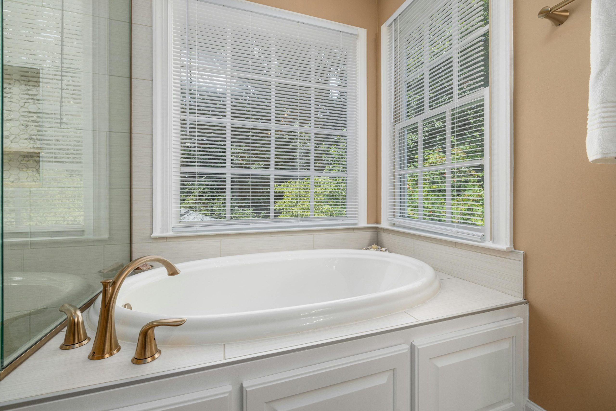 Bright bathroom featuring a white bathtub, brass faucets, and large windows with blinds.