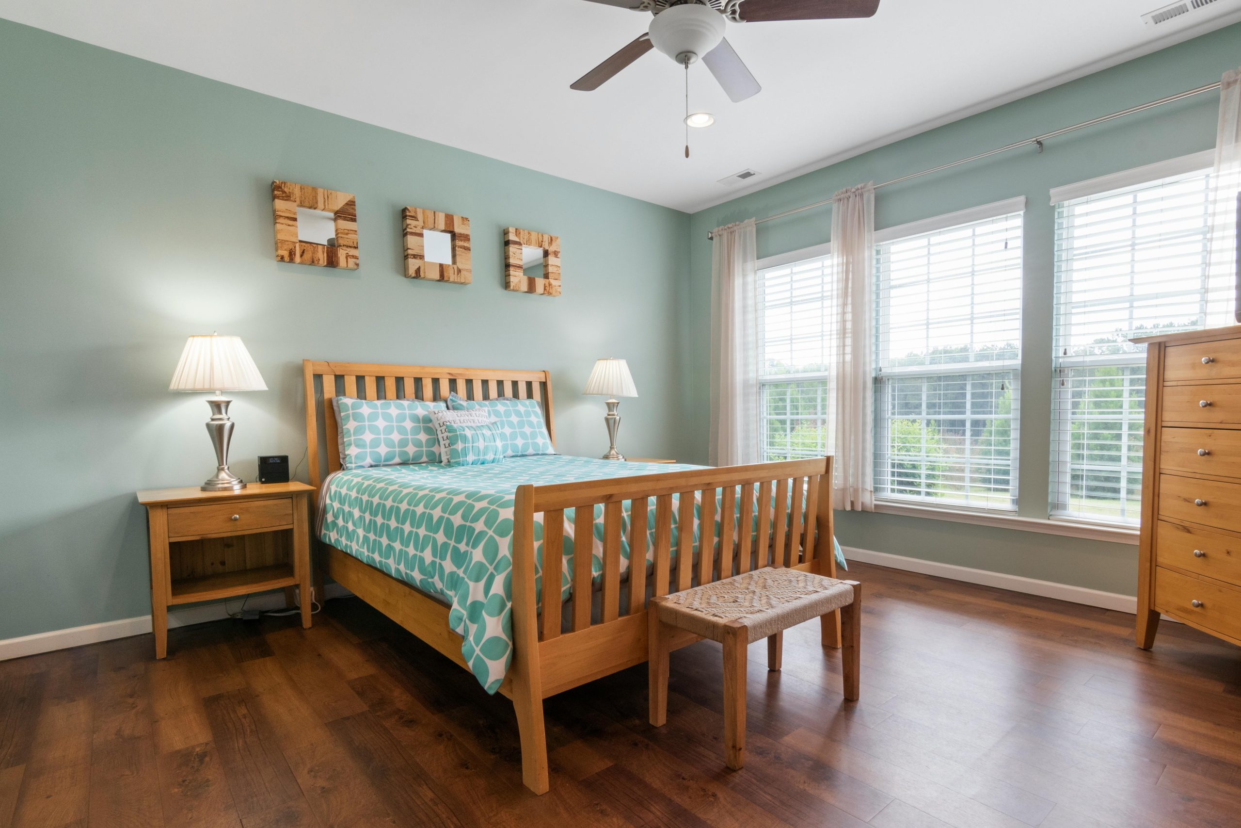 Bright bedroom with wooden furniture and mint green walls, featuring natural light.