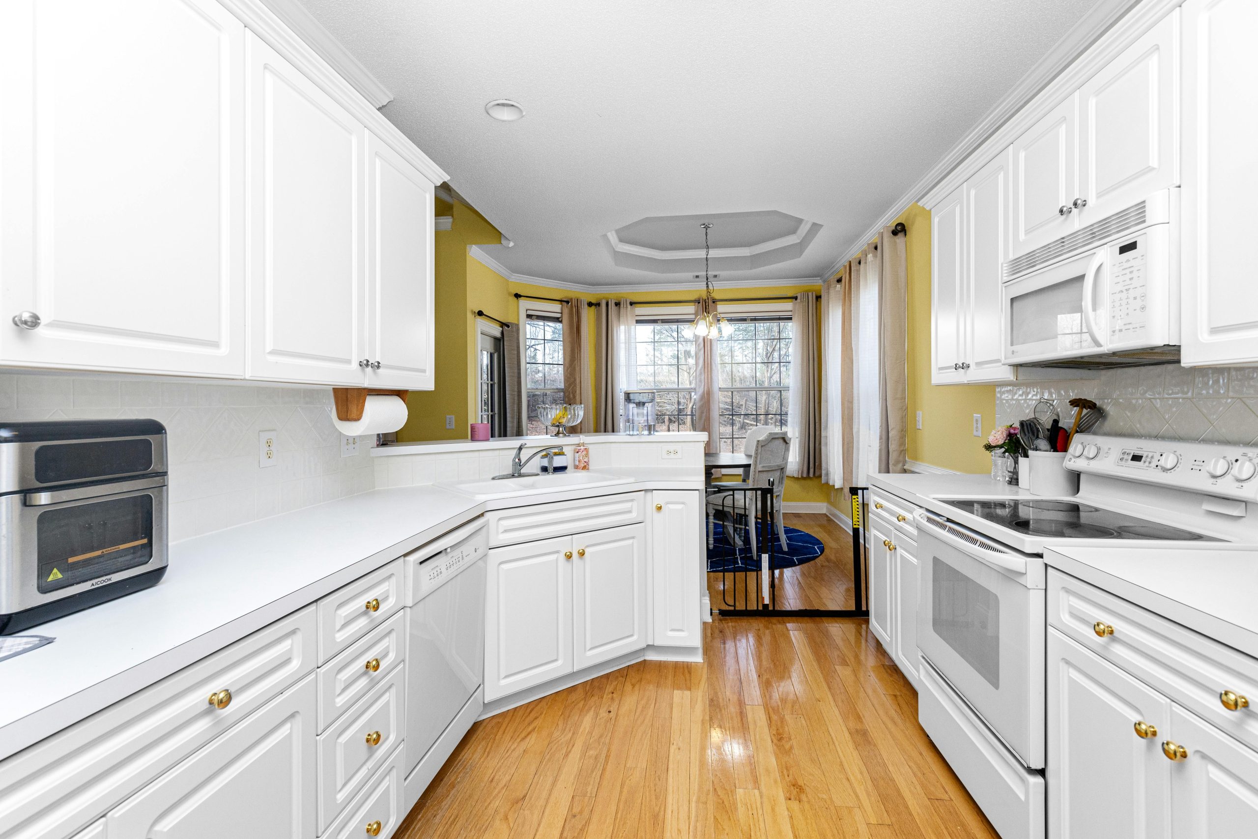 Bright modern kitchen with white cabinets, wooden floors, and stainless steel appliances.