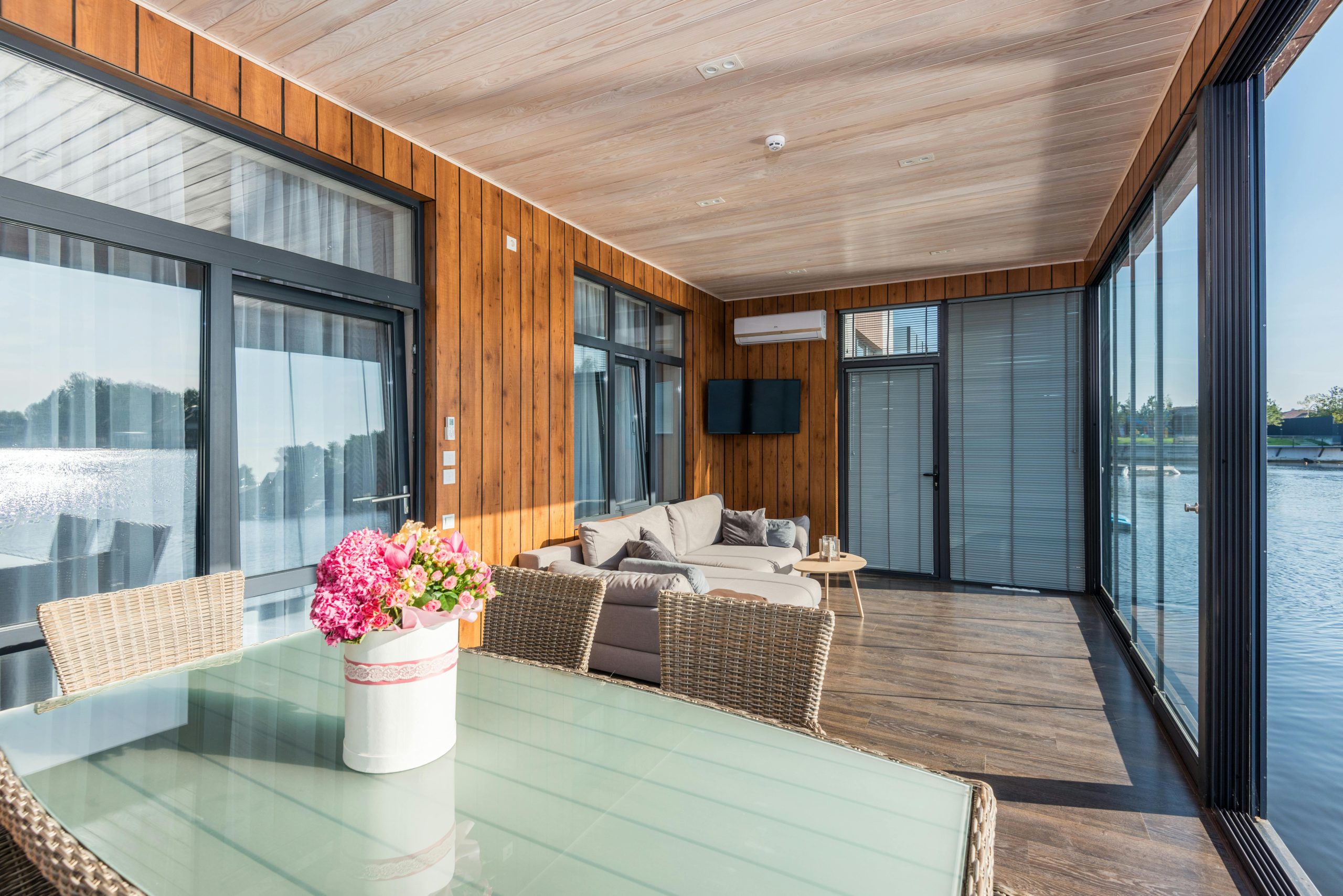 Bright sunroom with lake view, featuring wicker furniture and vibrant flowers.