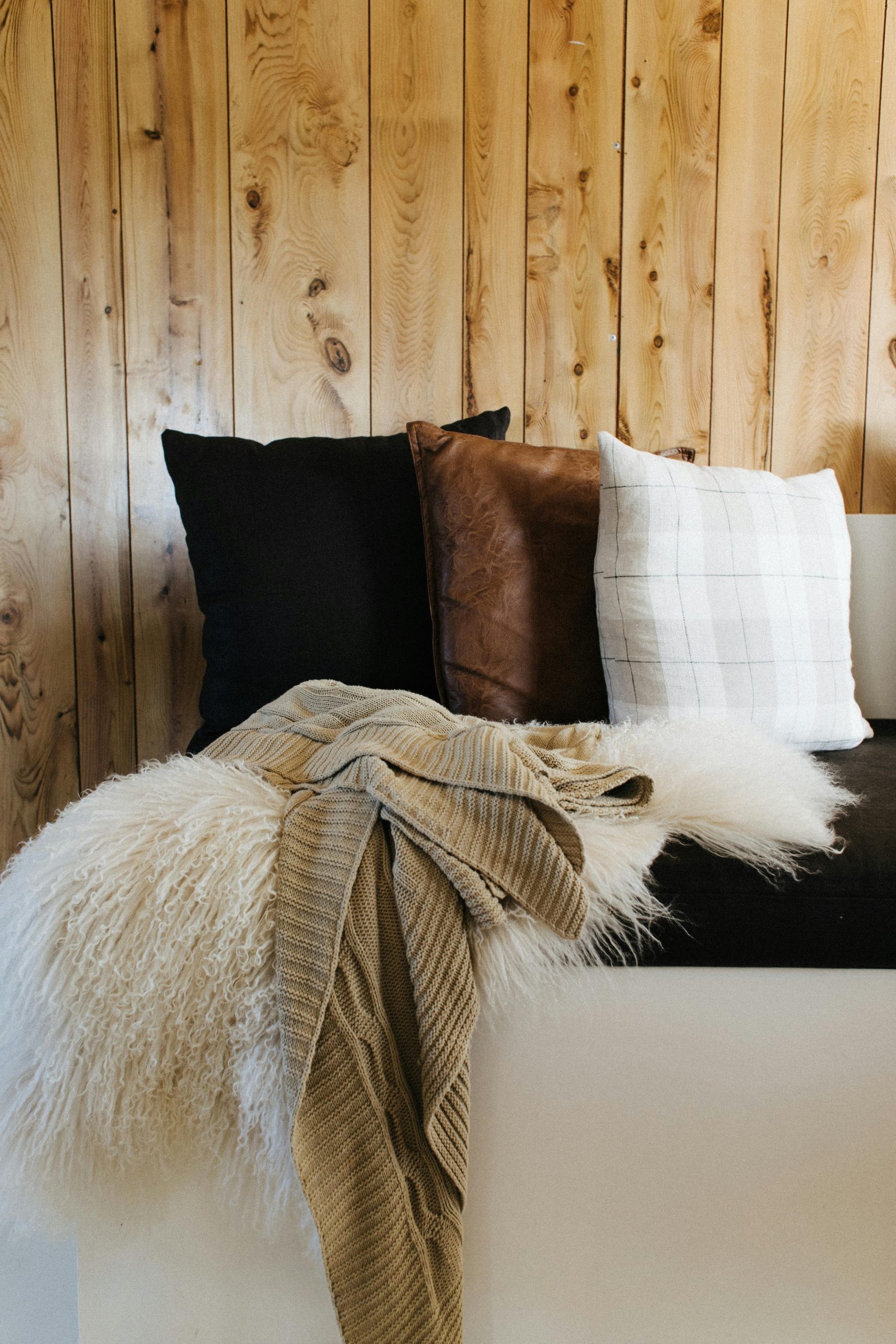 Comfortable white couch with soft colorful cushions and fluff and cotton plaids near wooden wall