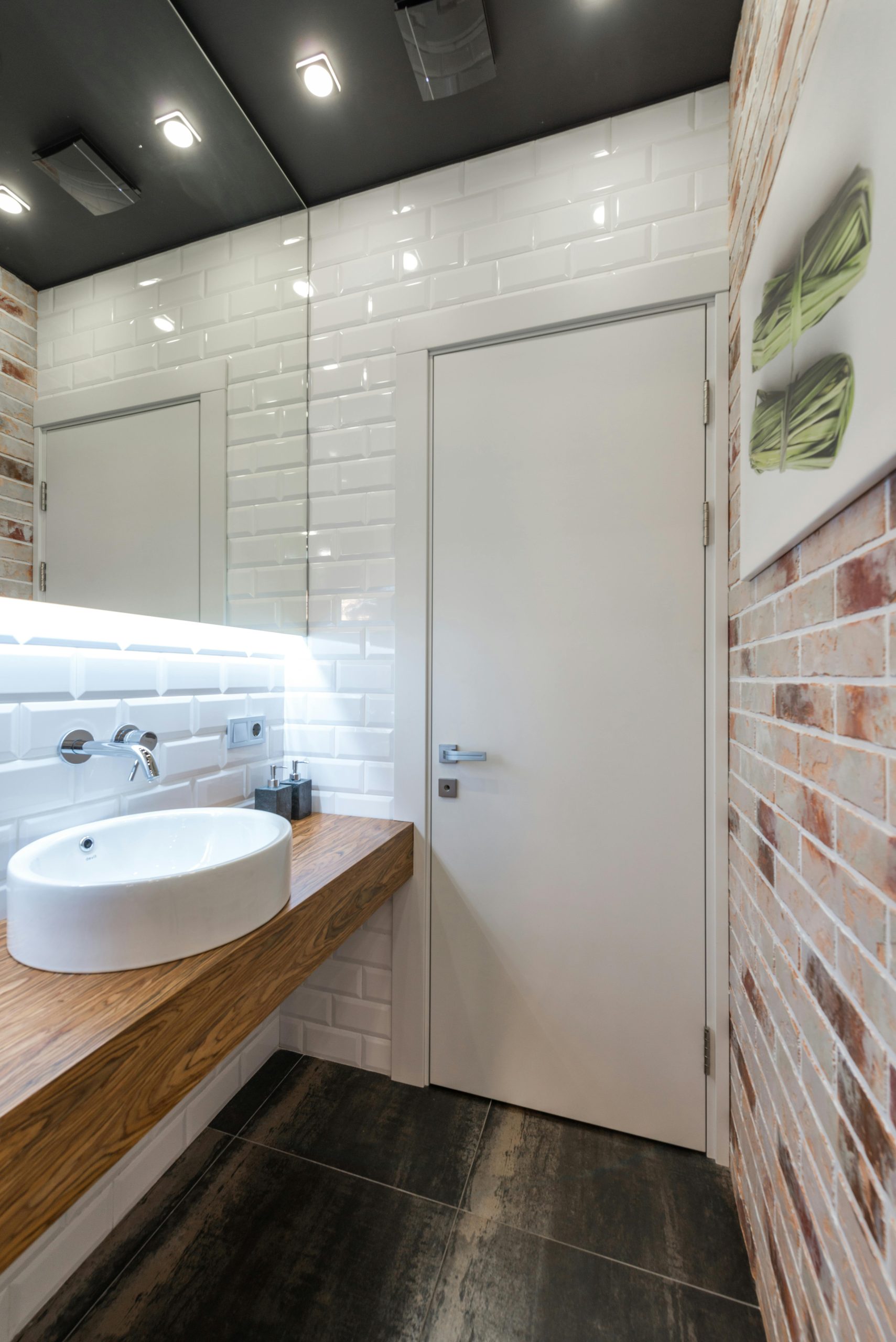 Contemporary bathroom featuring minimalist design with wooden counter, brick wall, and modern fixtures.