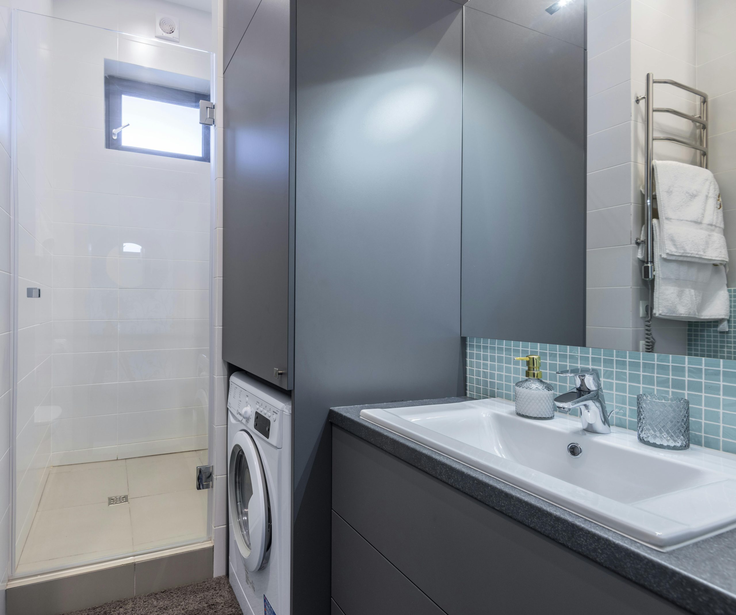Contemporary bathroom in an apartment featuring a washing machine, shower, and sleek decor.