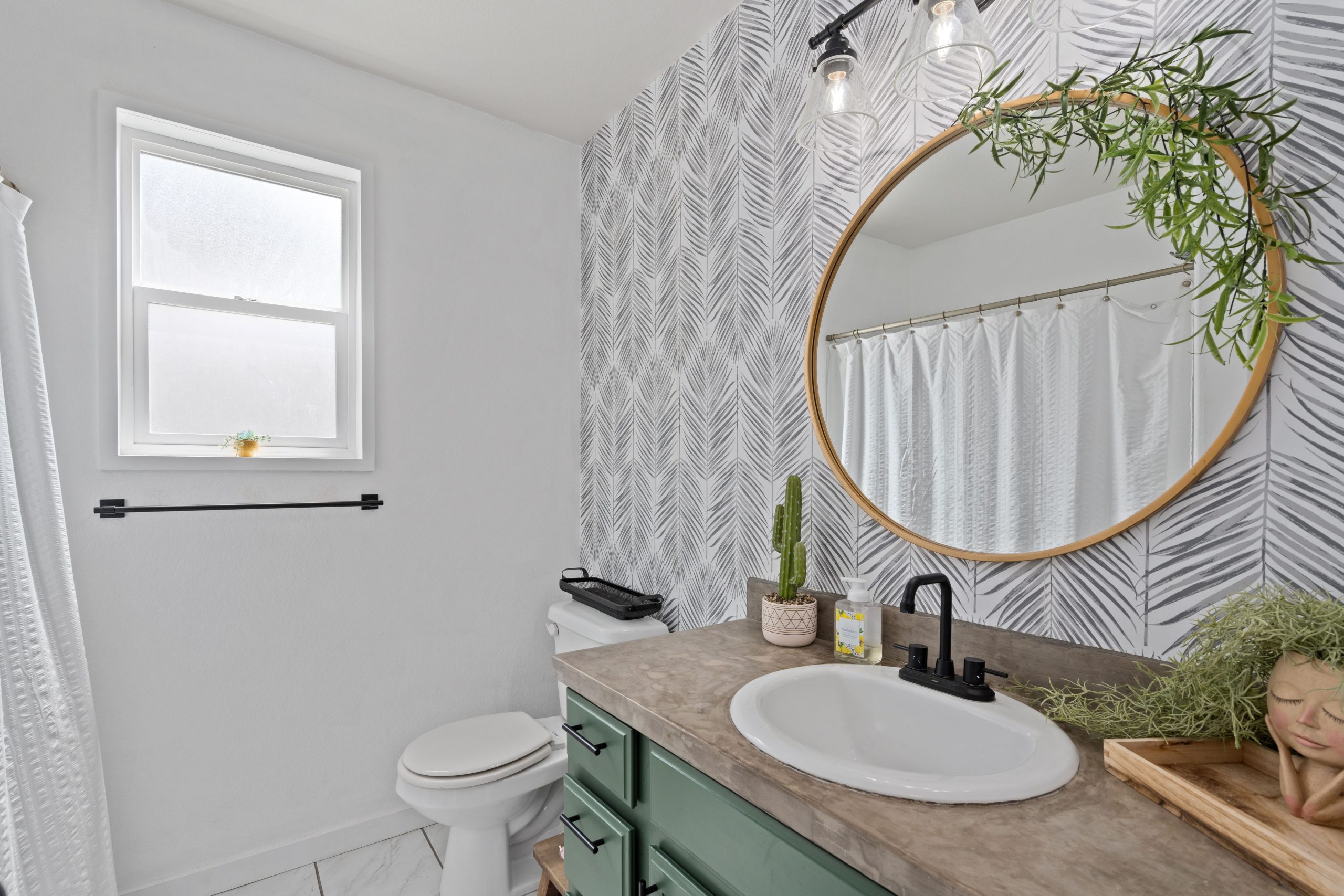 Contemporary bathroom with sleek design featuring mirror, green accents, and decorative plants.