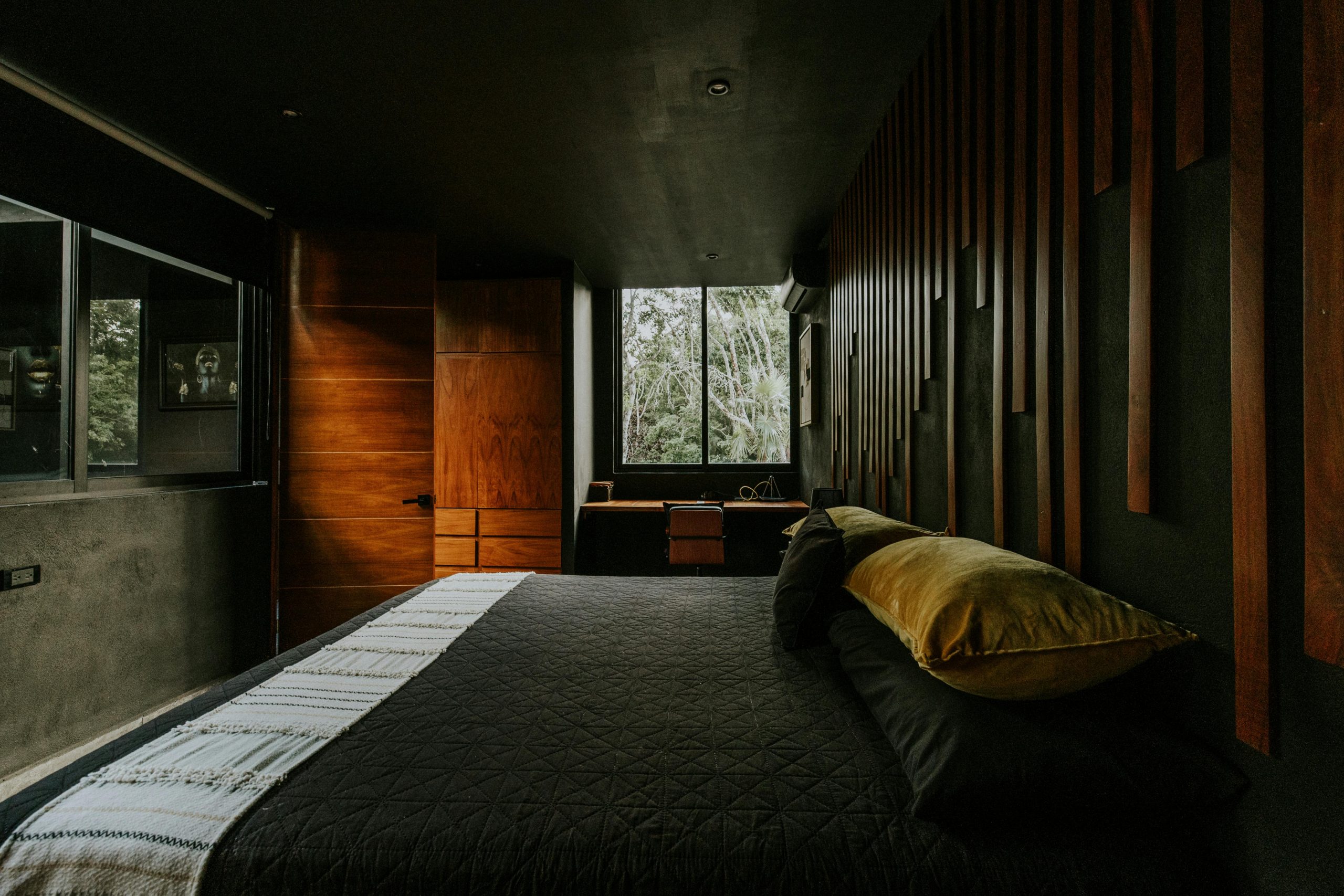 Contemporary bedroom with dark tones, wood accents, and a large window view.