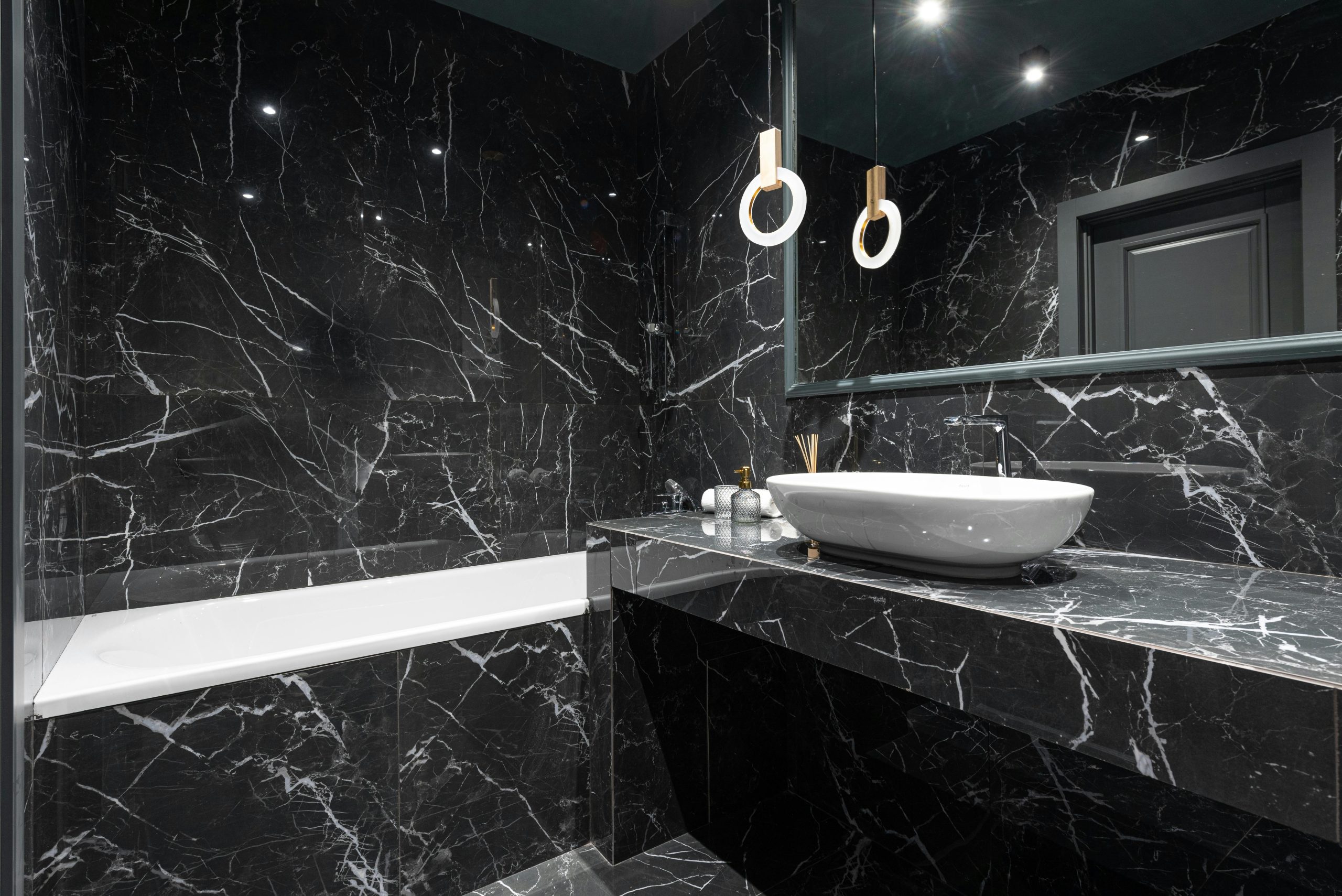 Contemporary interior design of bathroom with marble gray till on walls and stylish lamp reflecting in mirror above sink