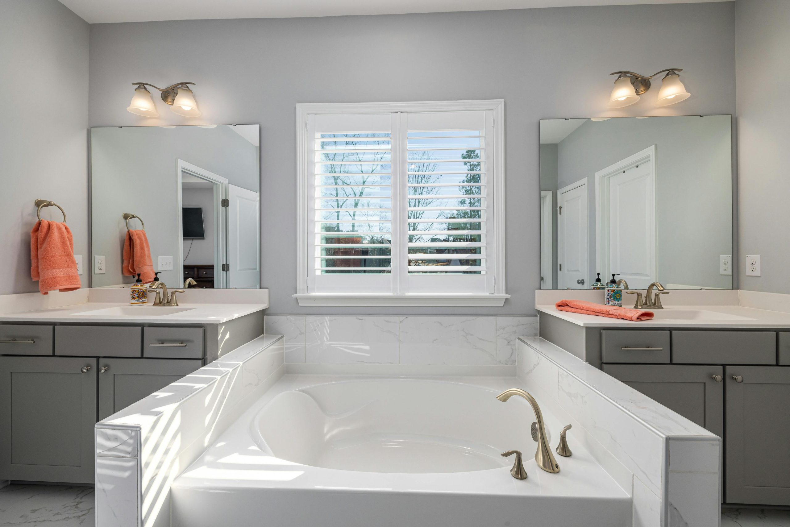 Elegant bathroom featuring a double vanity, bathtub, and natural light through window blinds.