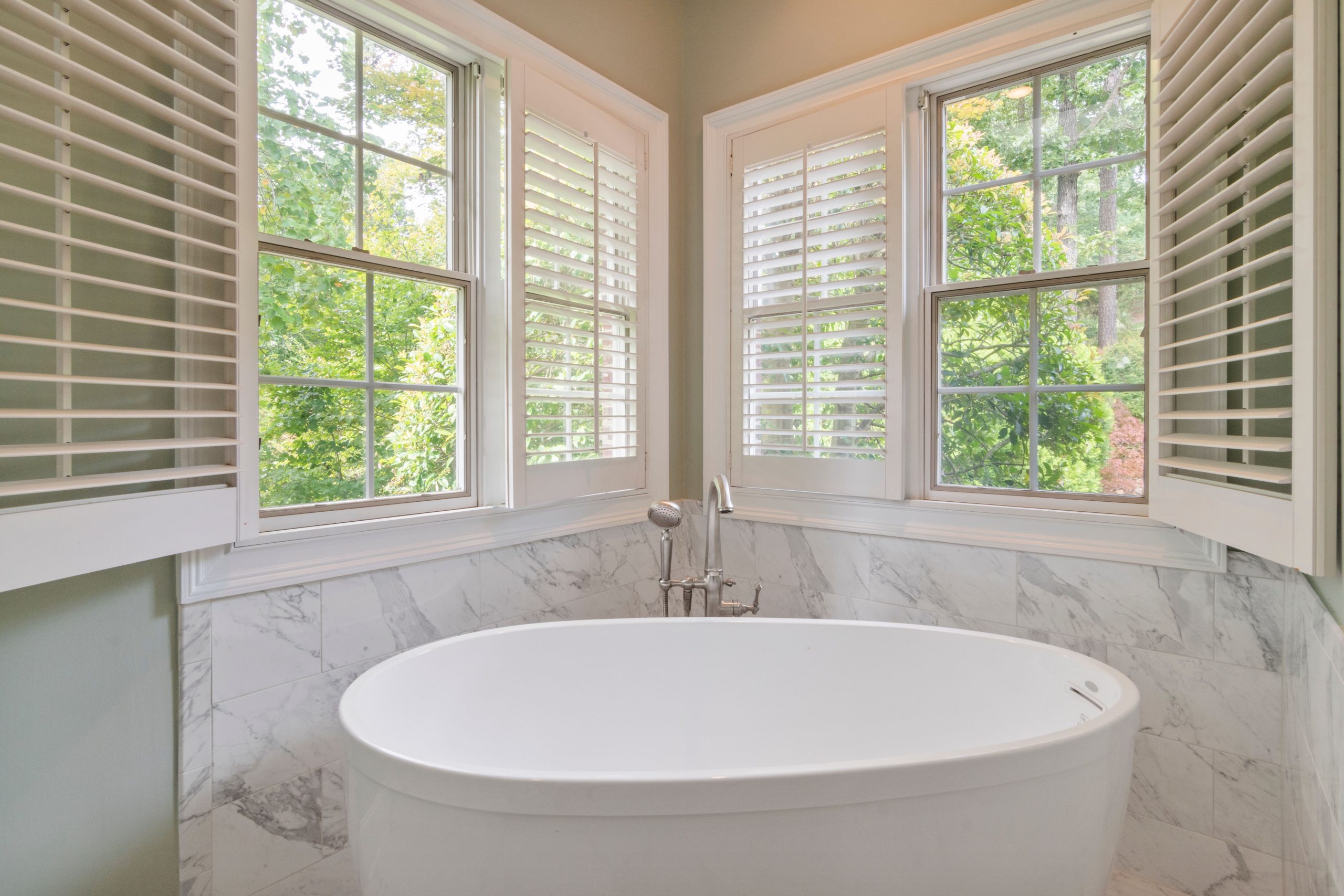 Elegant bathroom featuring a marble design and a freestanding tub, with natural light flooding through large windows.