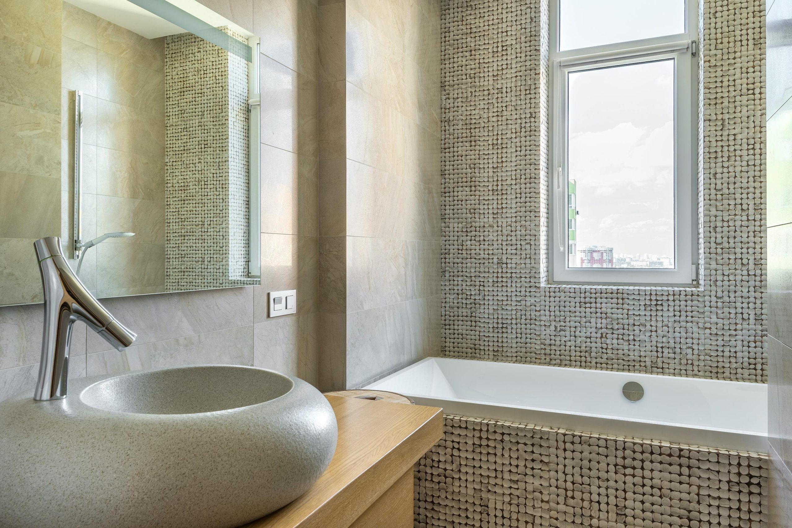 Elegant bathroom featuring a stone sink, modern faucet, and stylish bathtub with mosaic tiles.