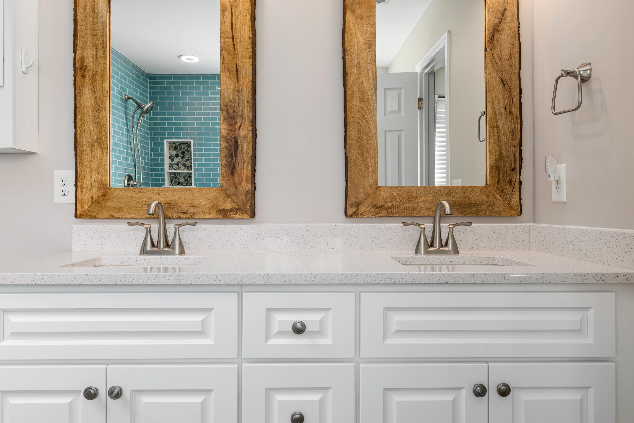 Elegant bathroom featuring double sinks, wooden mirrors, and blue tiled shower.