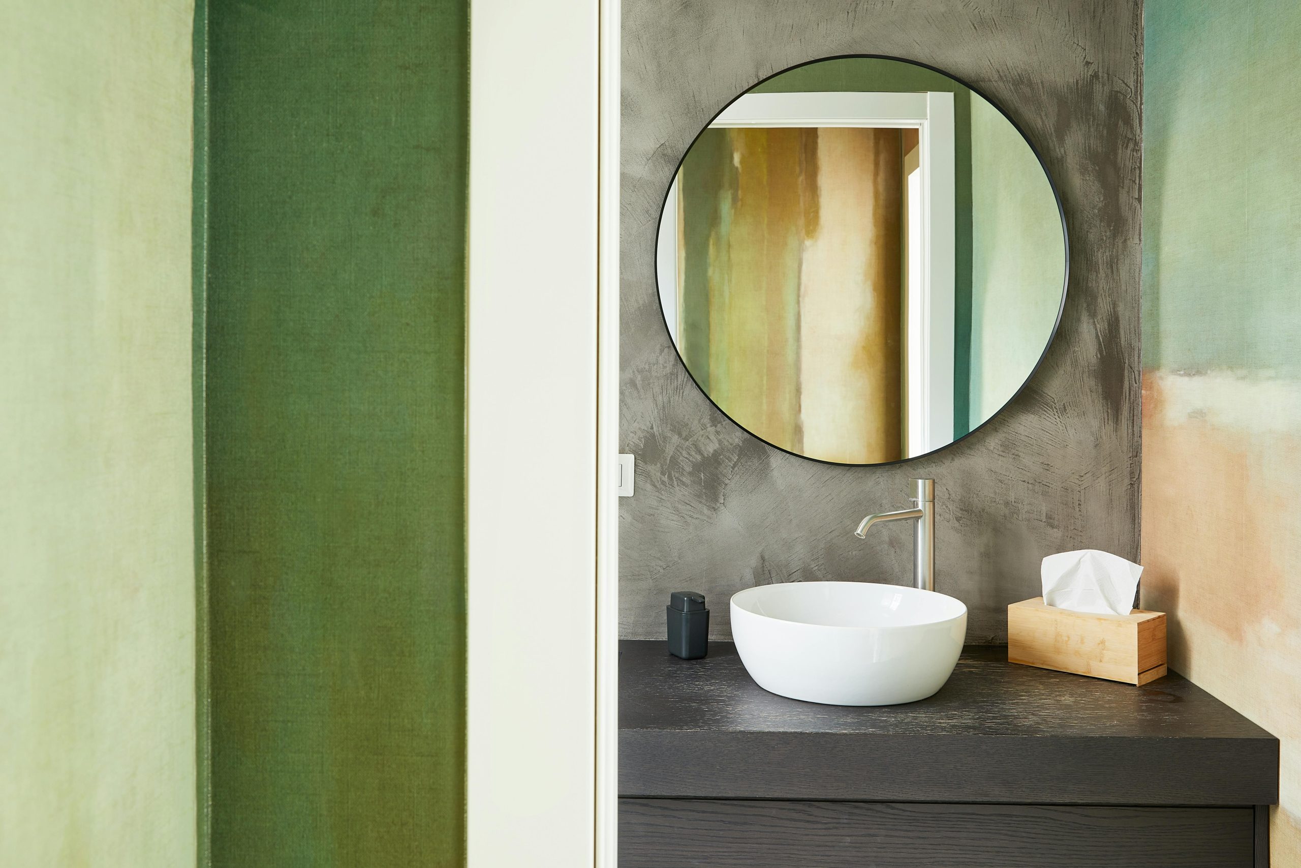 Elegant bathroom featuring green walls, a sleek sink, and a round mirror for a modern touch.