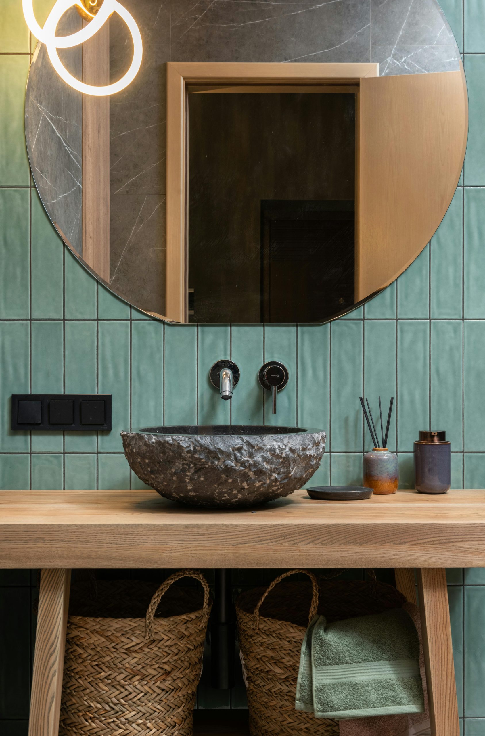 Elegant bathroom featuring stone basin, round mirror, and green tiles.