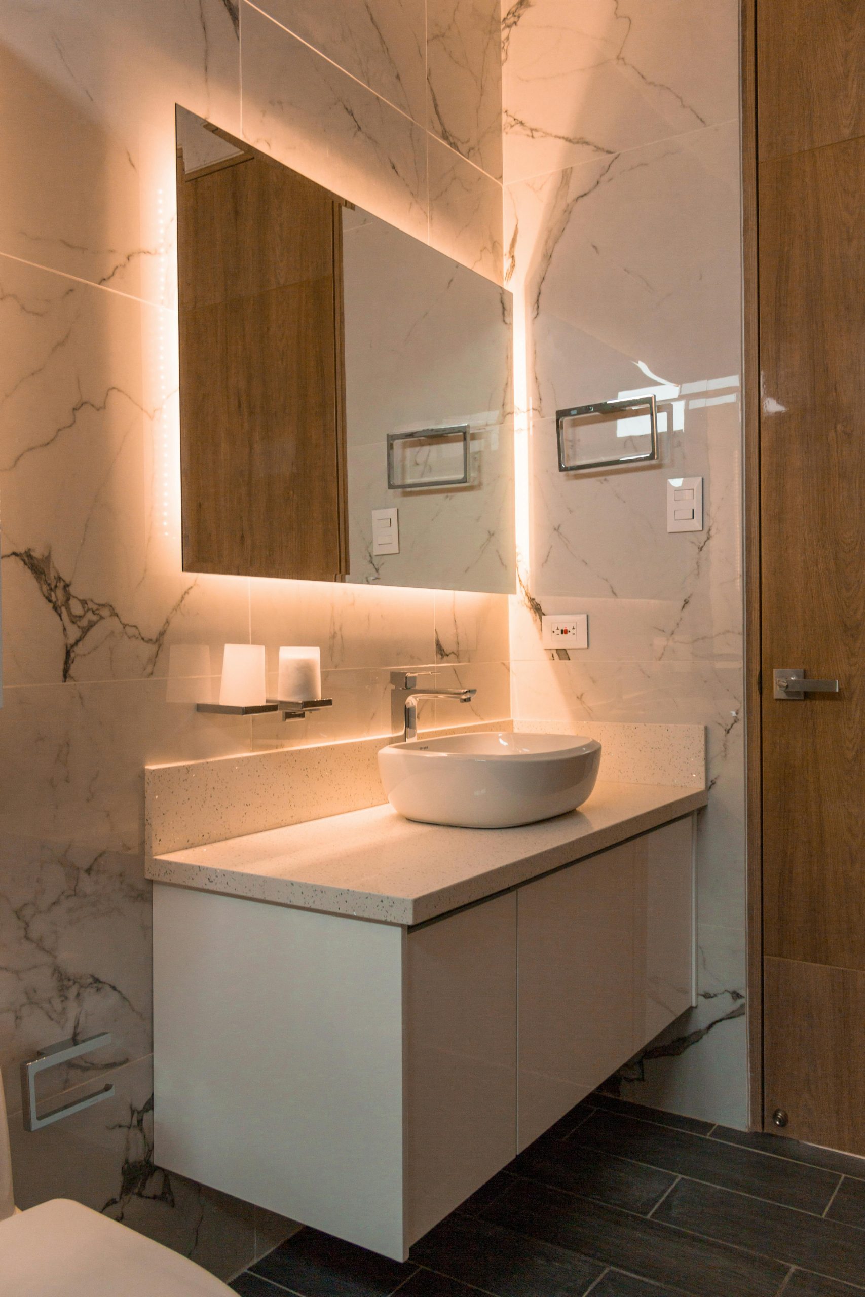 Elegant bathroom showcasing a contemporary sink, illuminated mirror, and marble tiles for a luxurious interior.